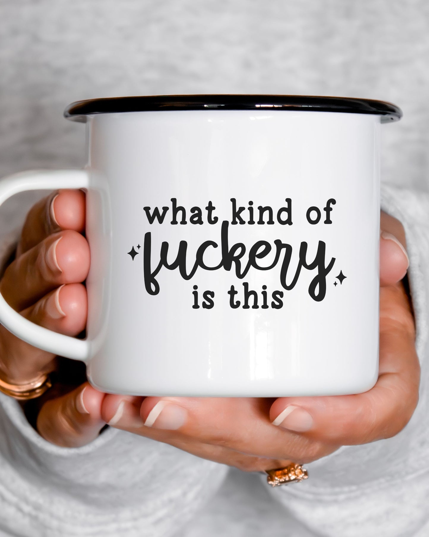Person holding a white mug with black text 'what kind of fuckery is this' against a neutral background