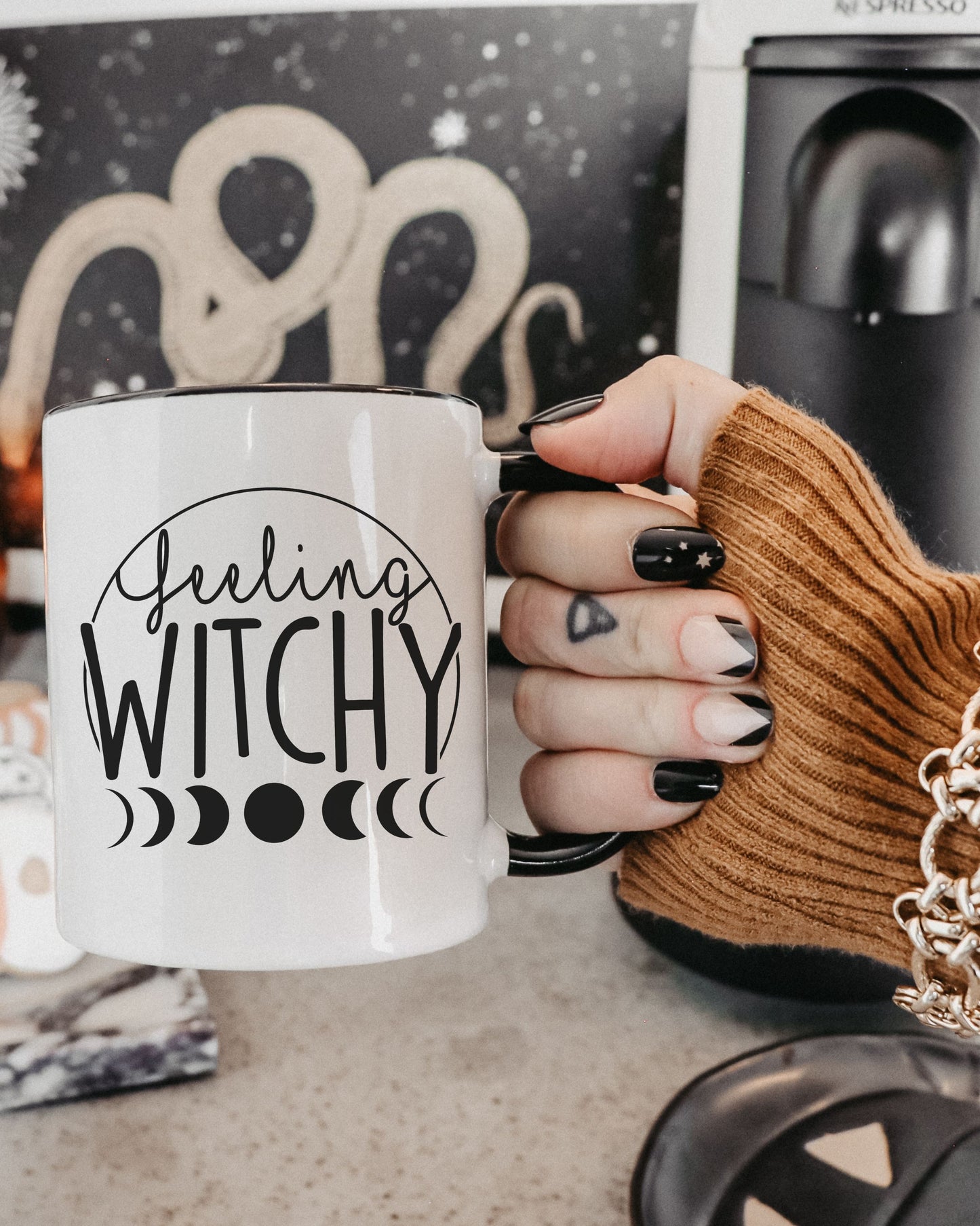 Hand holding a mug with 'Feeling Witchy' text in front of a coffee maker.
