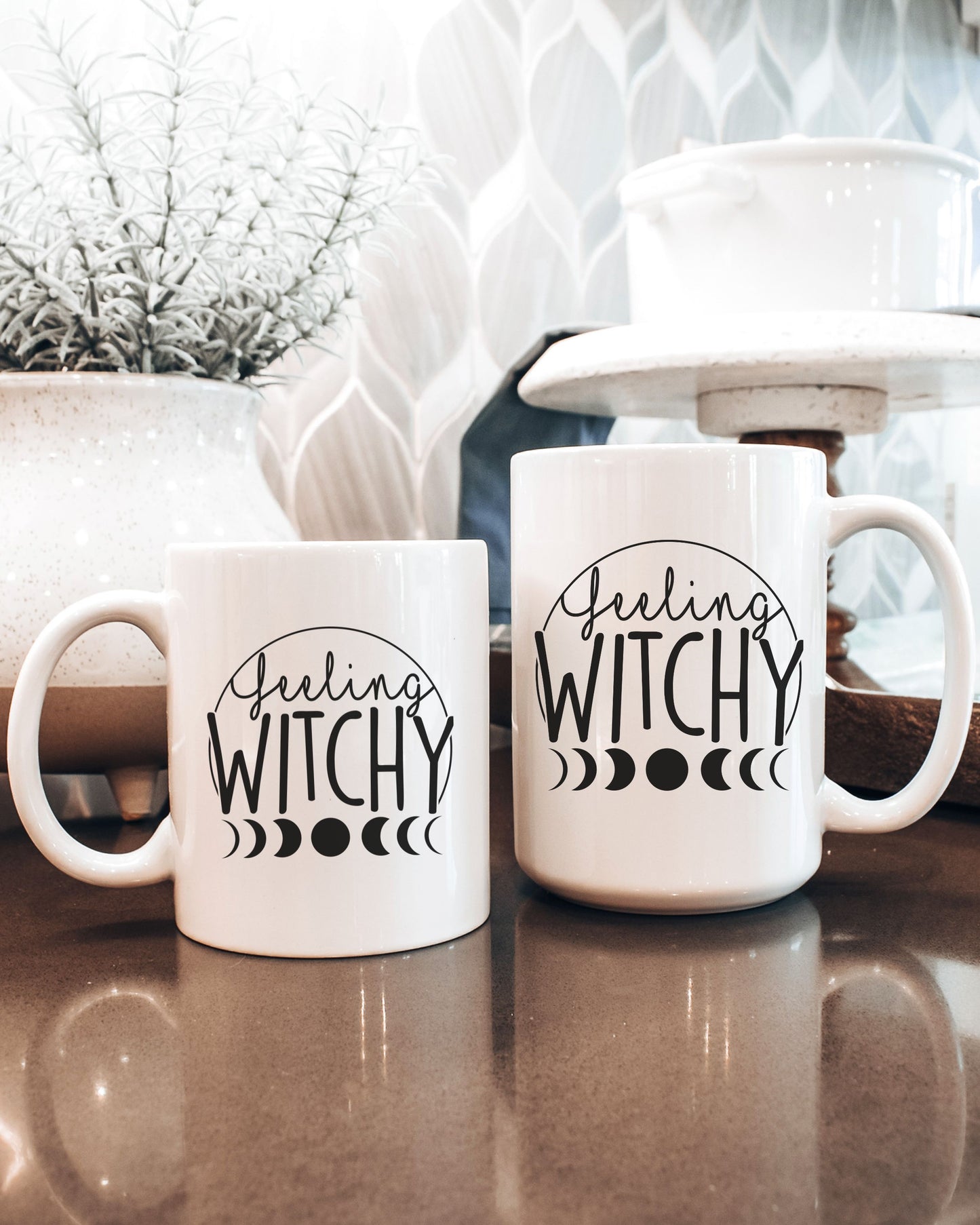 Two white mugs with 'Feeling Witchy' text on a kitchen counter.