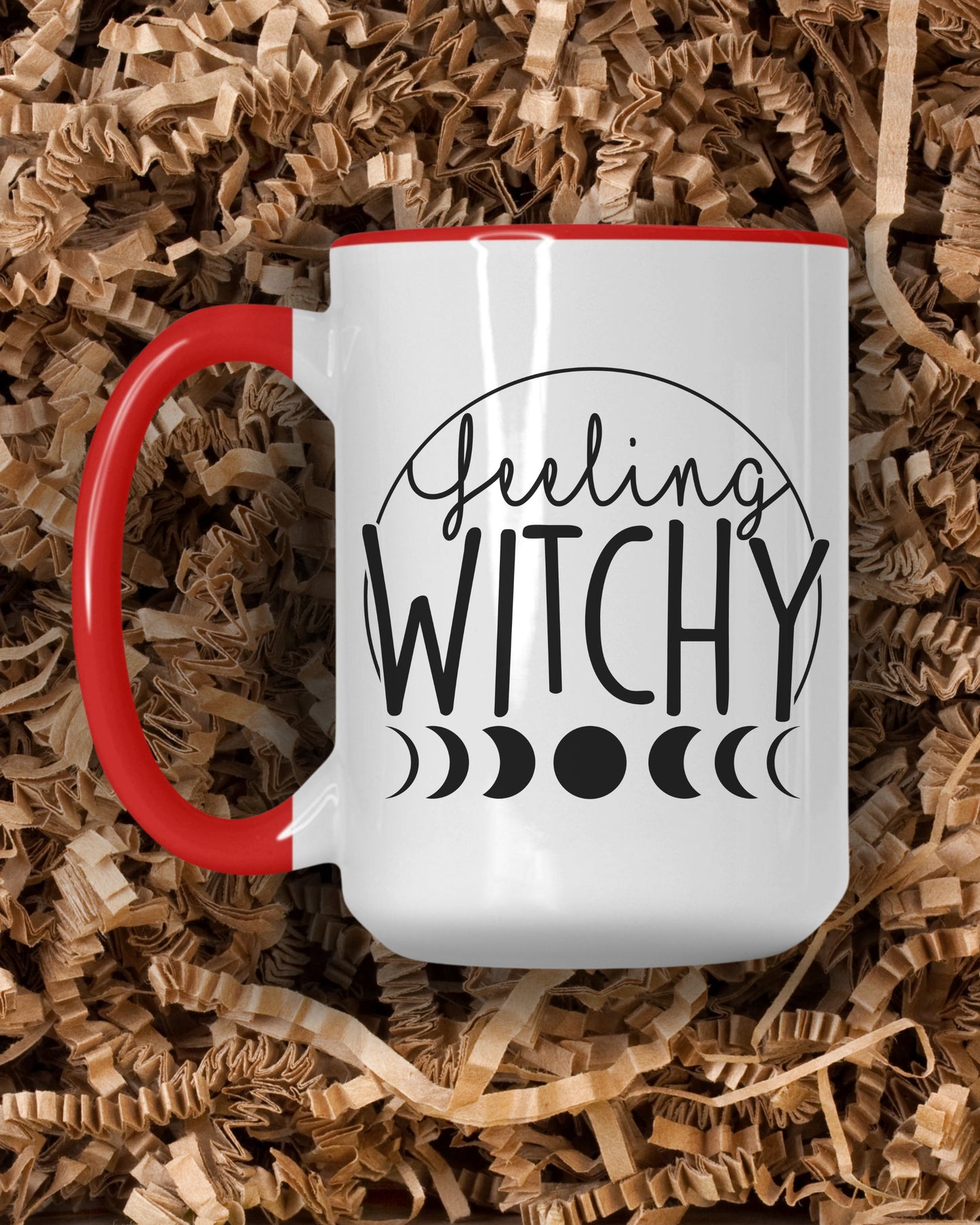 White mug with red handle featuring 'Feeling Witchy' text on a bed of crinkle paper shreds