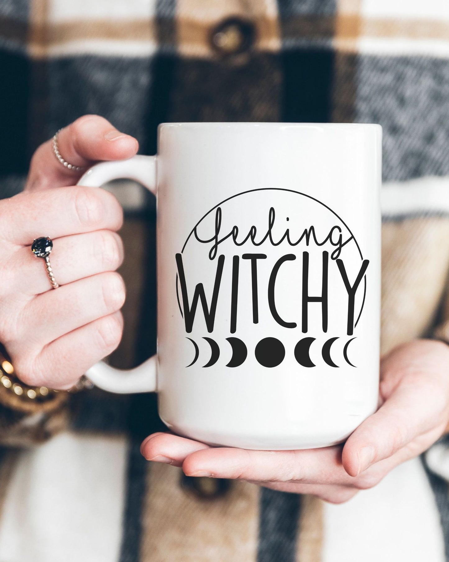 Person holding a white mug with 'Feeling Witchy' text and moon phases design.