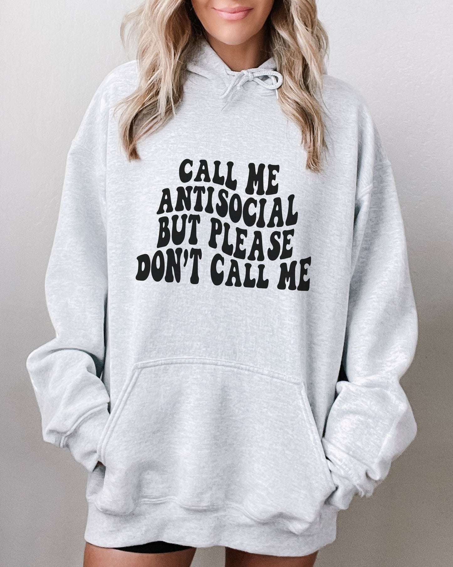 Gray hoodie with text 'Call me antisocial but please don't call me' worn by a person.