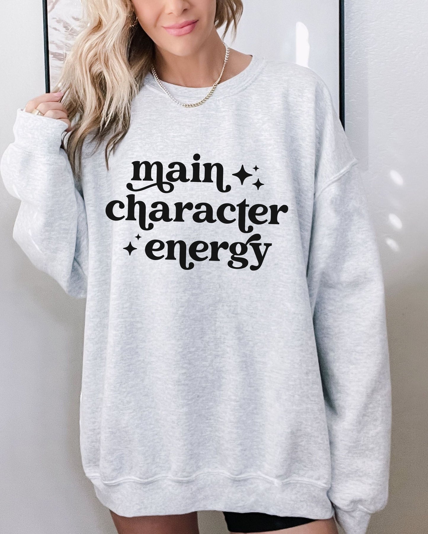 Person wearing a gray sweatshirt with 'main character energy' text.