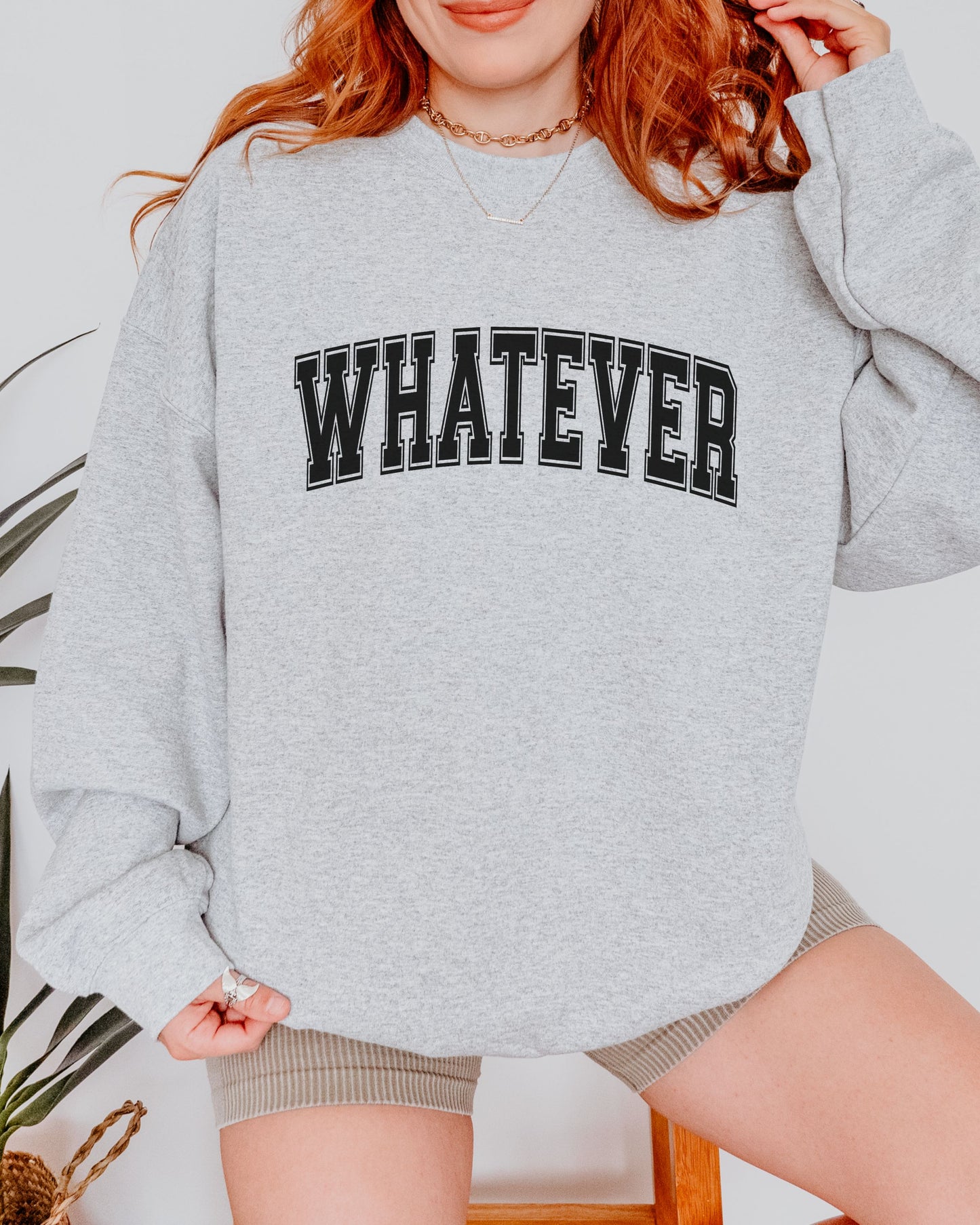 Person wearing a gray sweatshirt with 'WHATEVER' text, standing against a light background.
