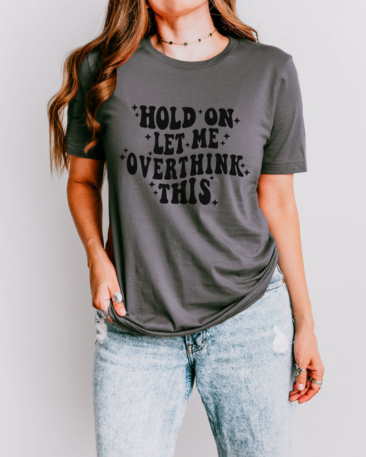 Person wearing a gray t-shirt with text 'Hold on, let me overthink this' on a plain background