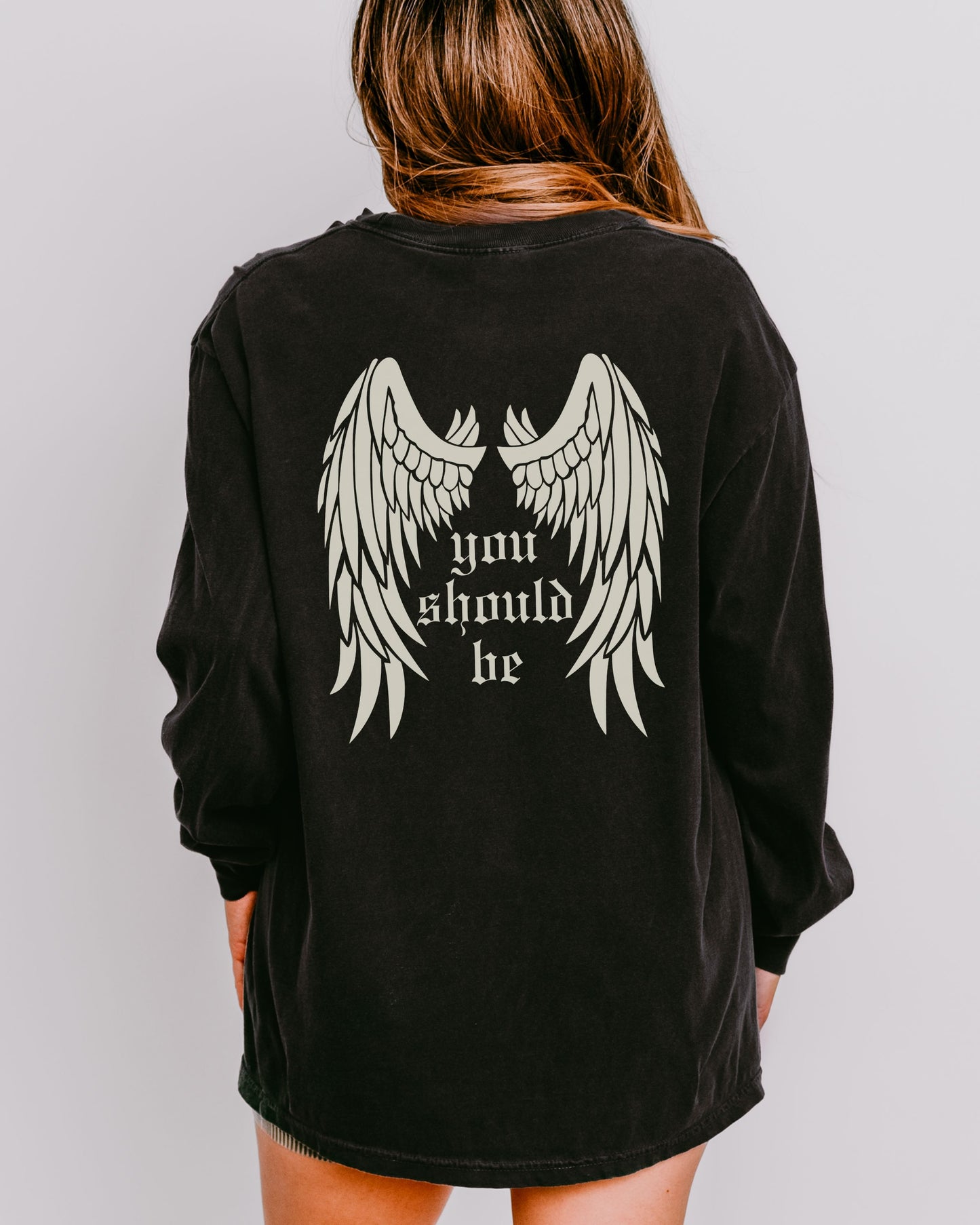 Black long-sleeve shirt with angel wings and text on the back, worn by a person against a plain background.