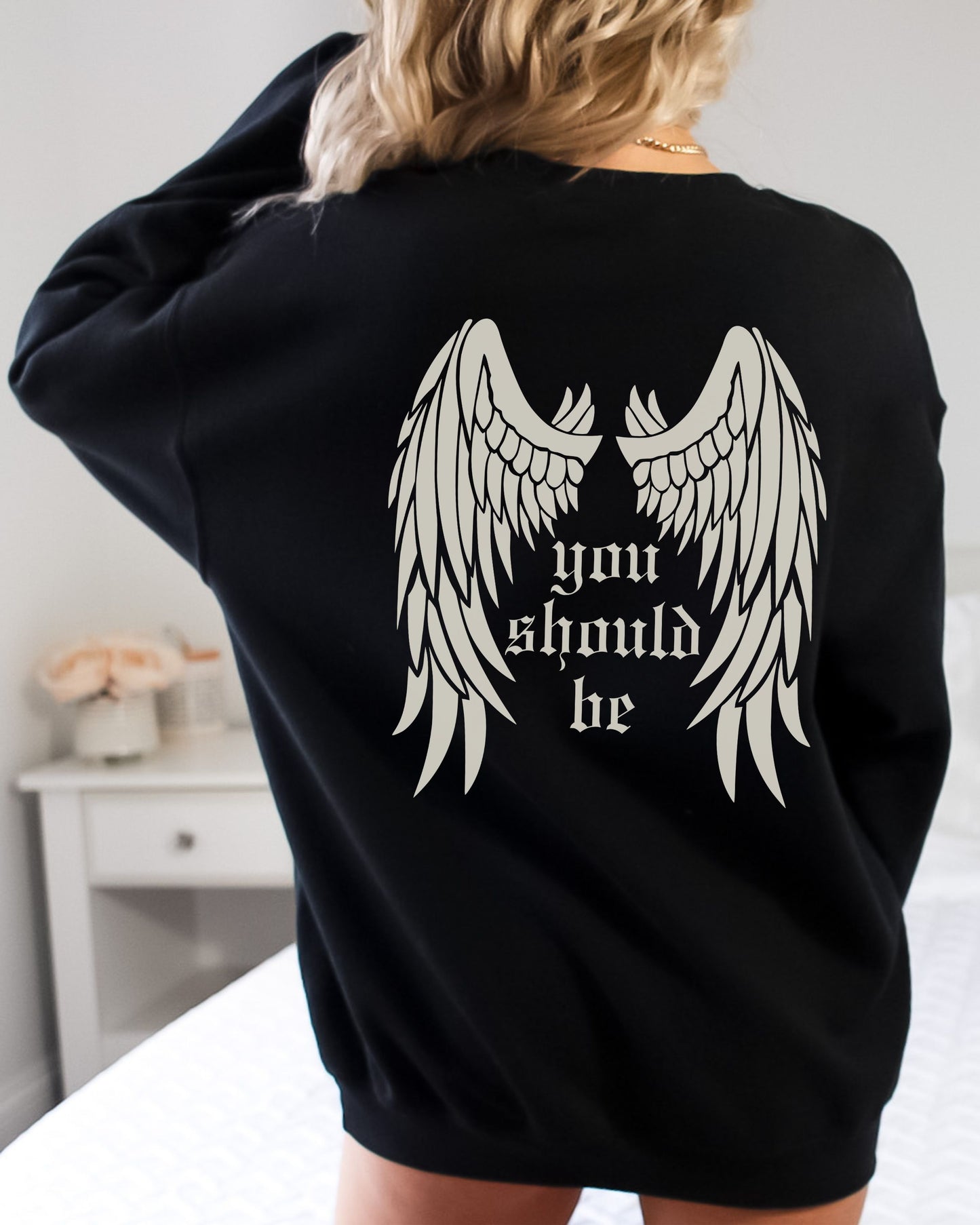Black sweatshirt with angel wings and text on the back, worn by a person.