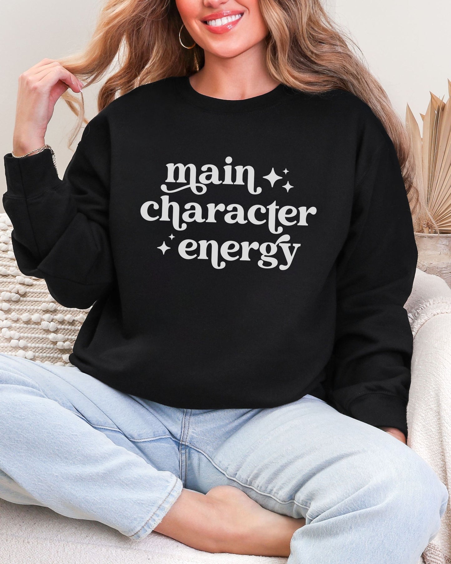 Person wearing a black sweatshirt with 'main character energy' text, sitting on a couch.