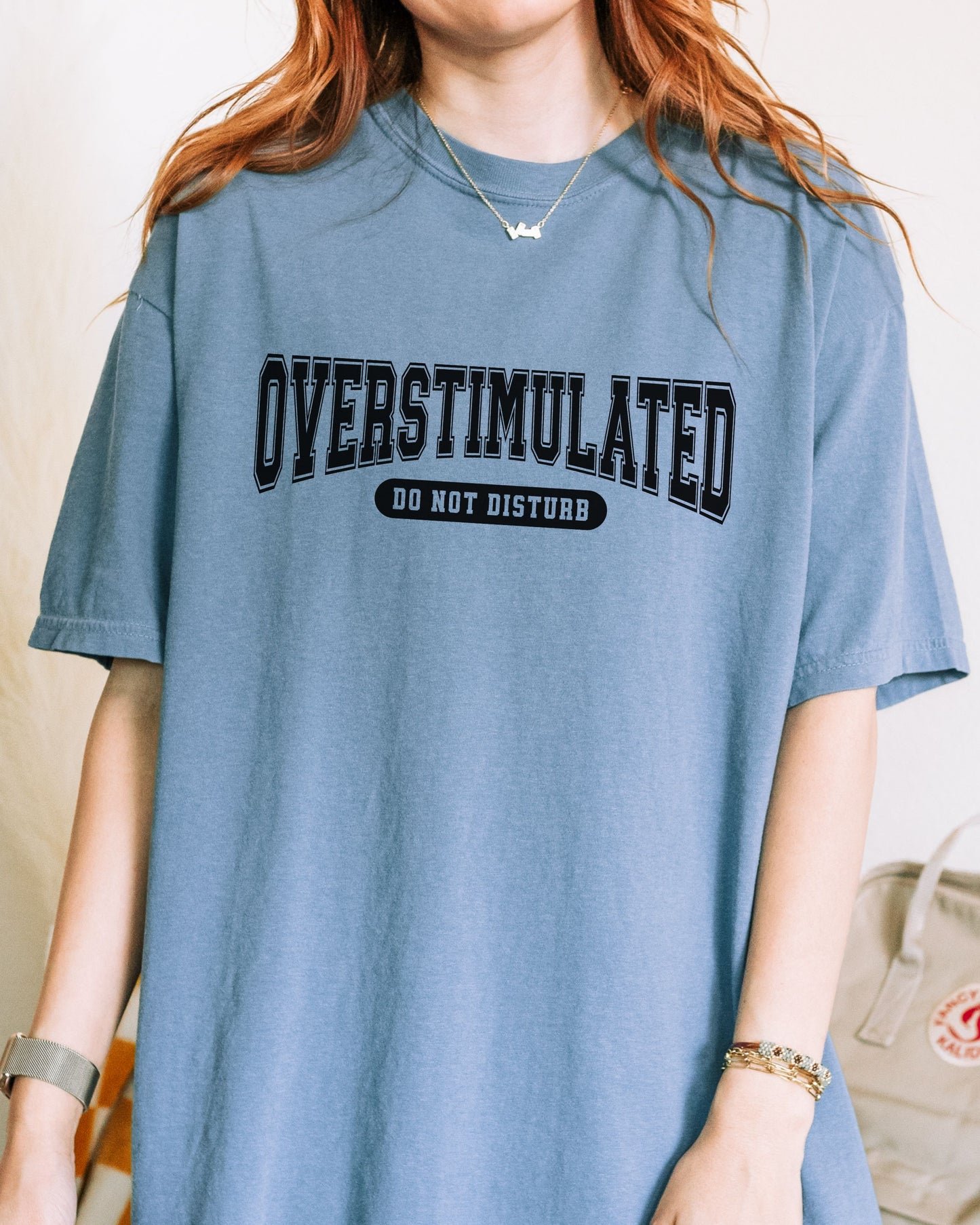 Person wearing a blue t-shirt with 'OVERSTIMULATED DO NOT DISTURB' text.