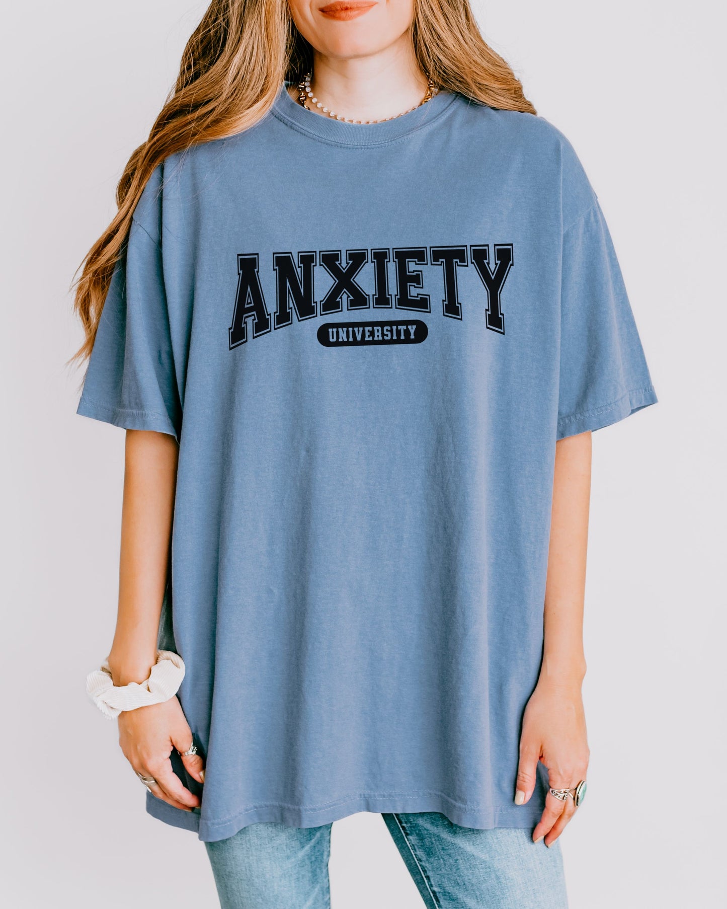 Person wearing a blue t-shirt with 'ANXIETY UNIVERSITY' text on a plain background