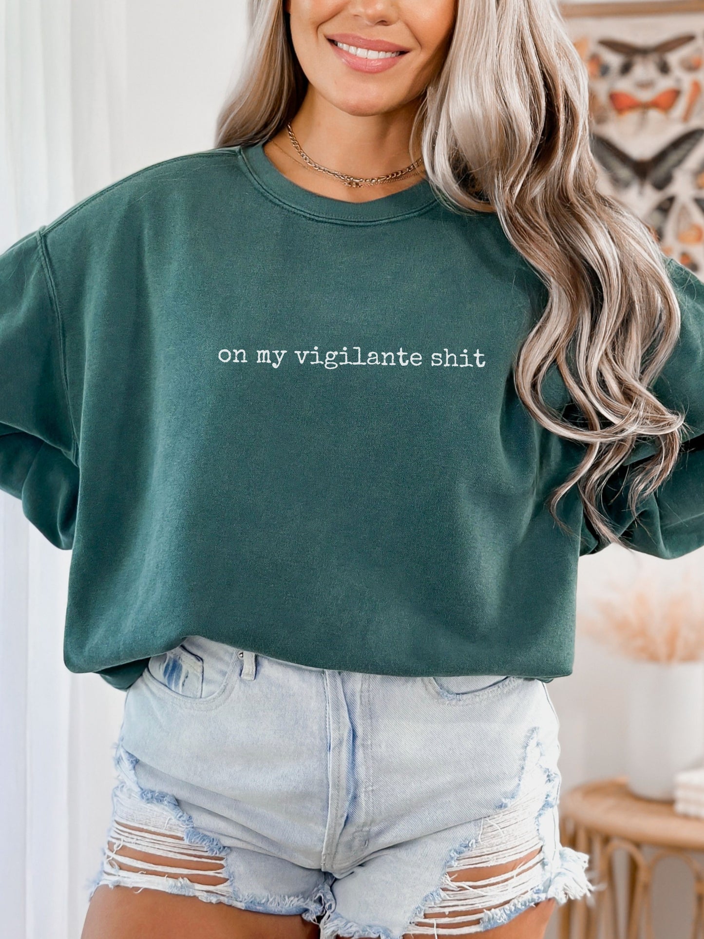 Person wearing a green sweatshirt with text and light blue shorts indoors.