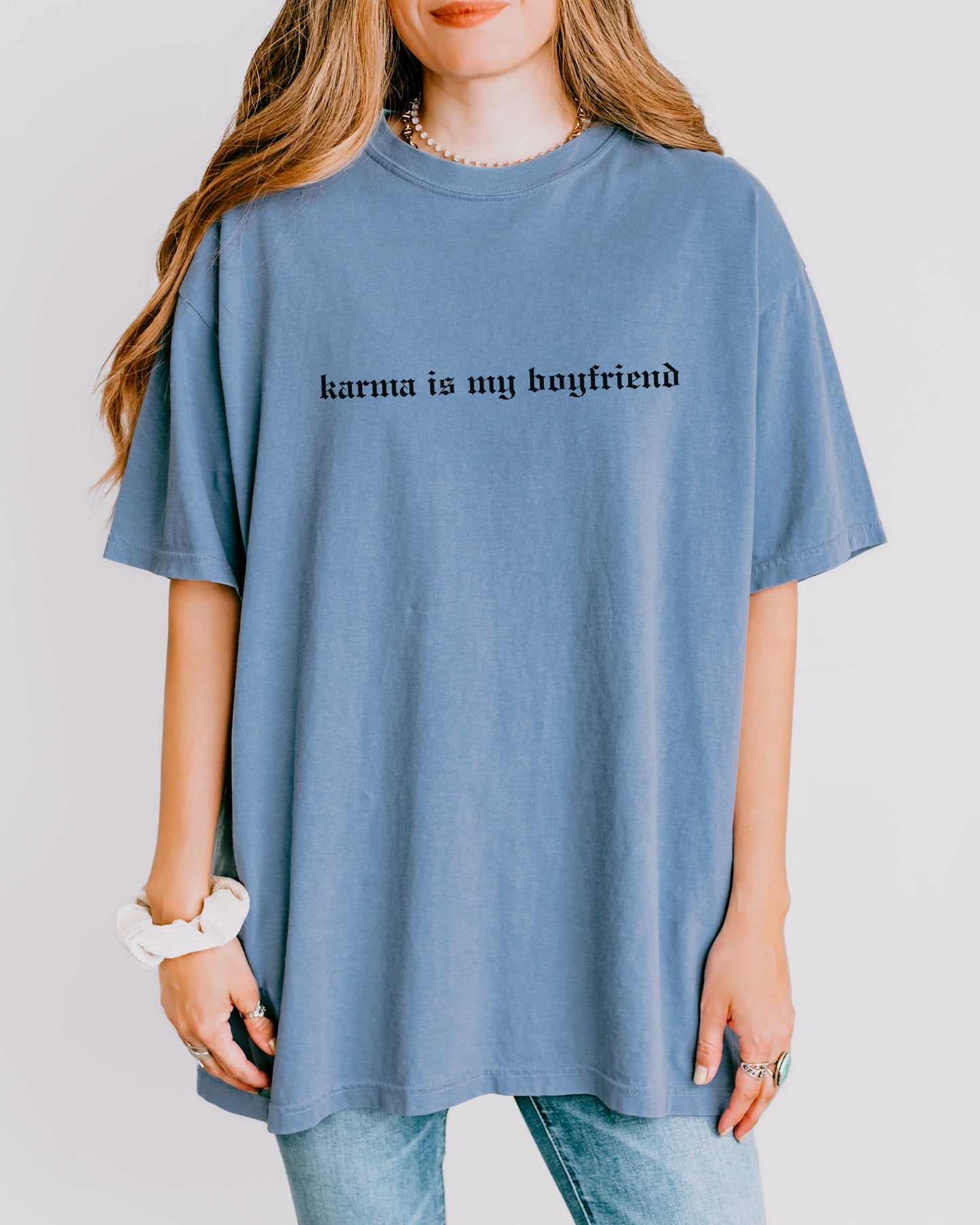 Person wearing a blue t-shirt with 'karma is my boyfriend' text on a plain background