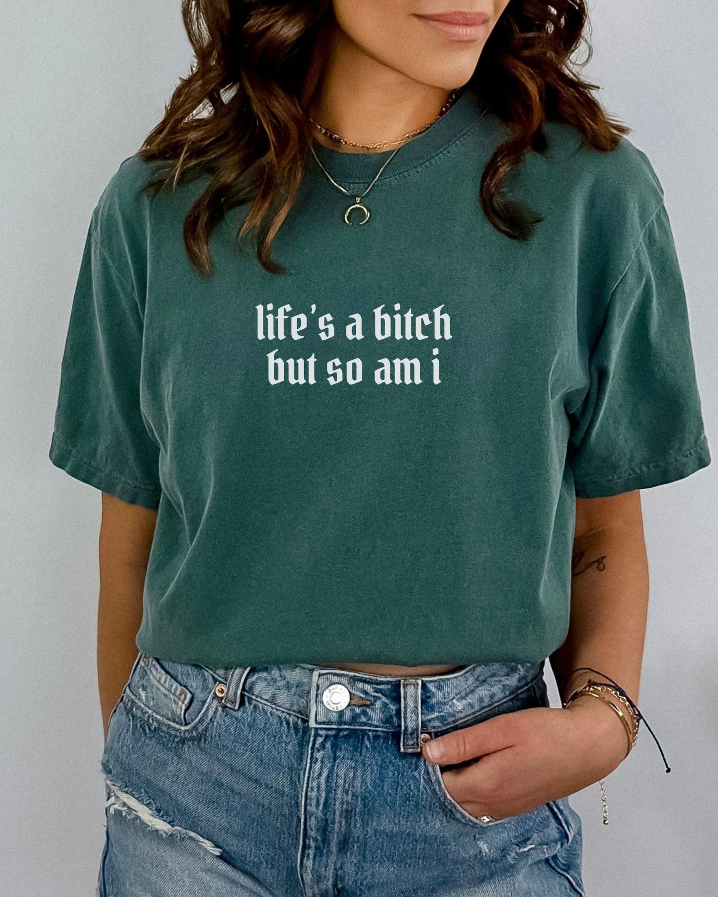 Person wearing a green t-shirt with text 'life's a bitch but so am i' on a plain background