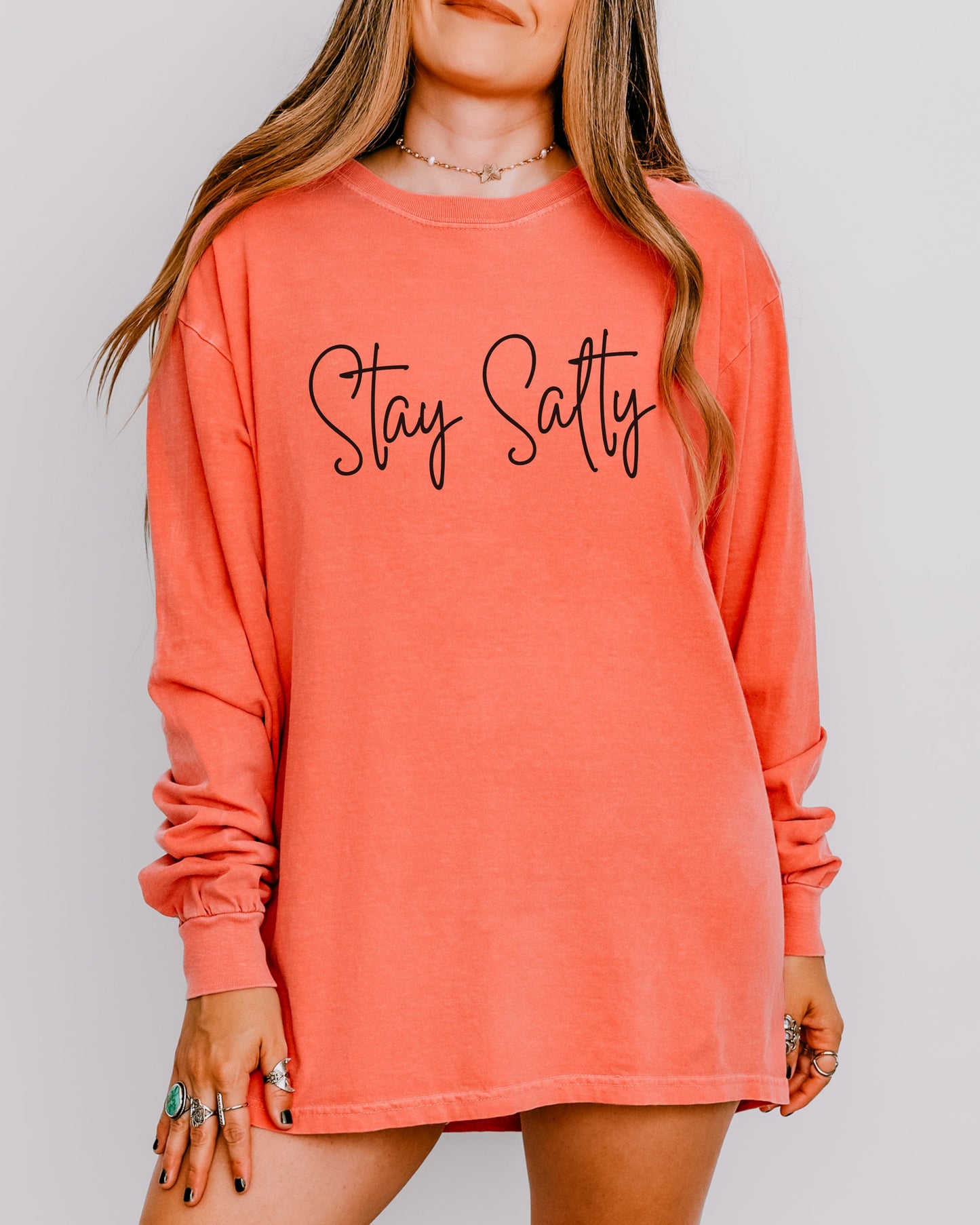 Person wearing a coral long-sleeve shirt with 'Stay Satty' text on a plain background