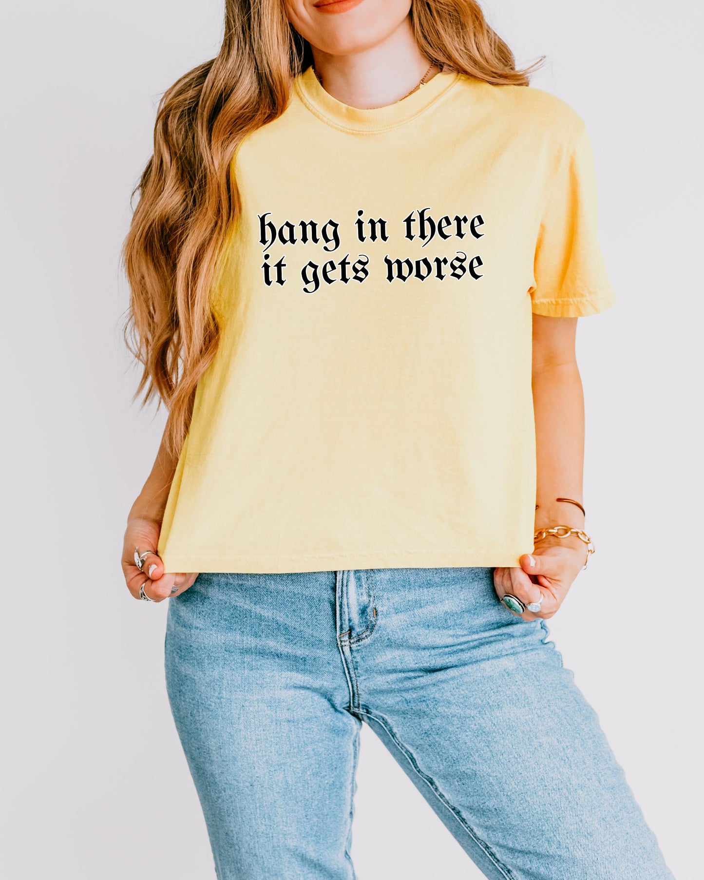 Person wearing a yellow t-shirt with text 'hang in there it gets worse' on a plain background