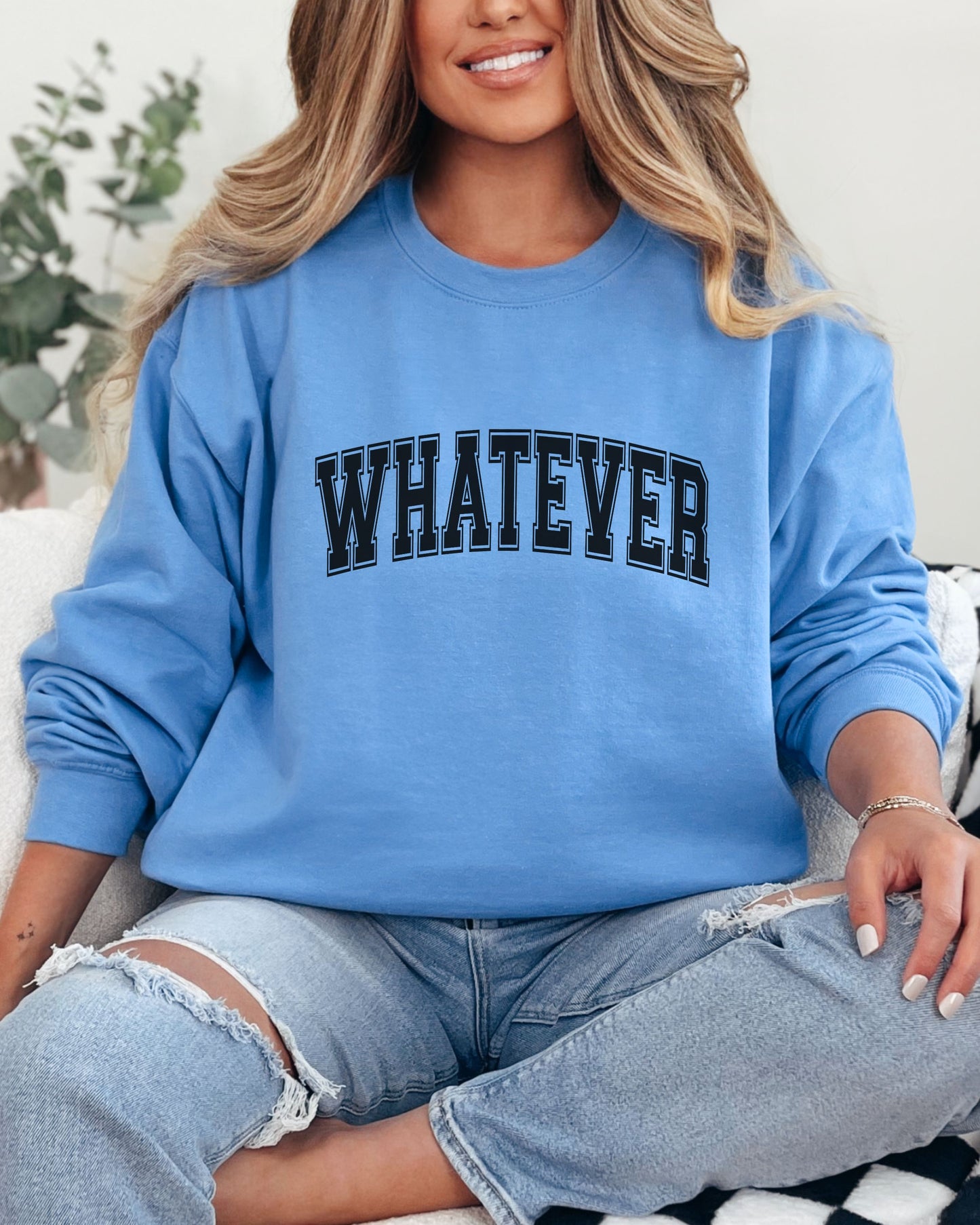 Person wearing a blue sweatshirt with 'WHATEVER' text, sitting on a checkered blanket.