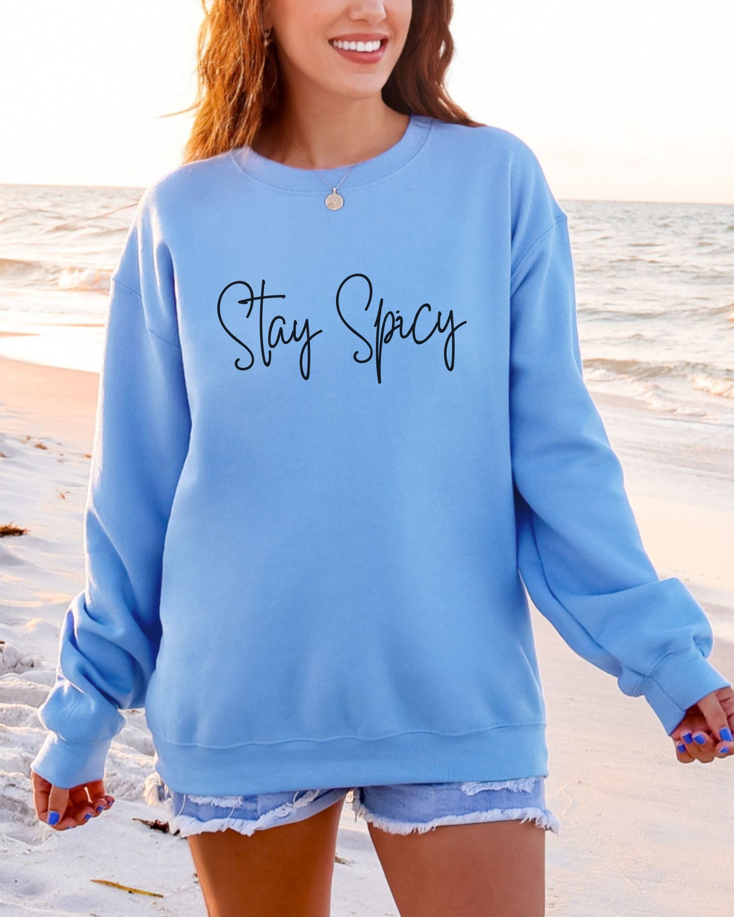 Person wearing a blue sweatshirt with 'Stay Spicy' text on a beach.