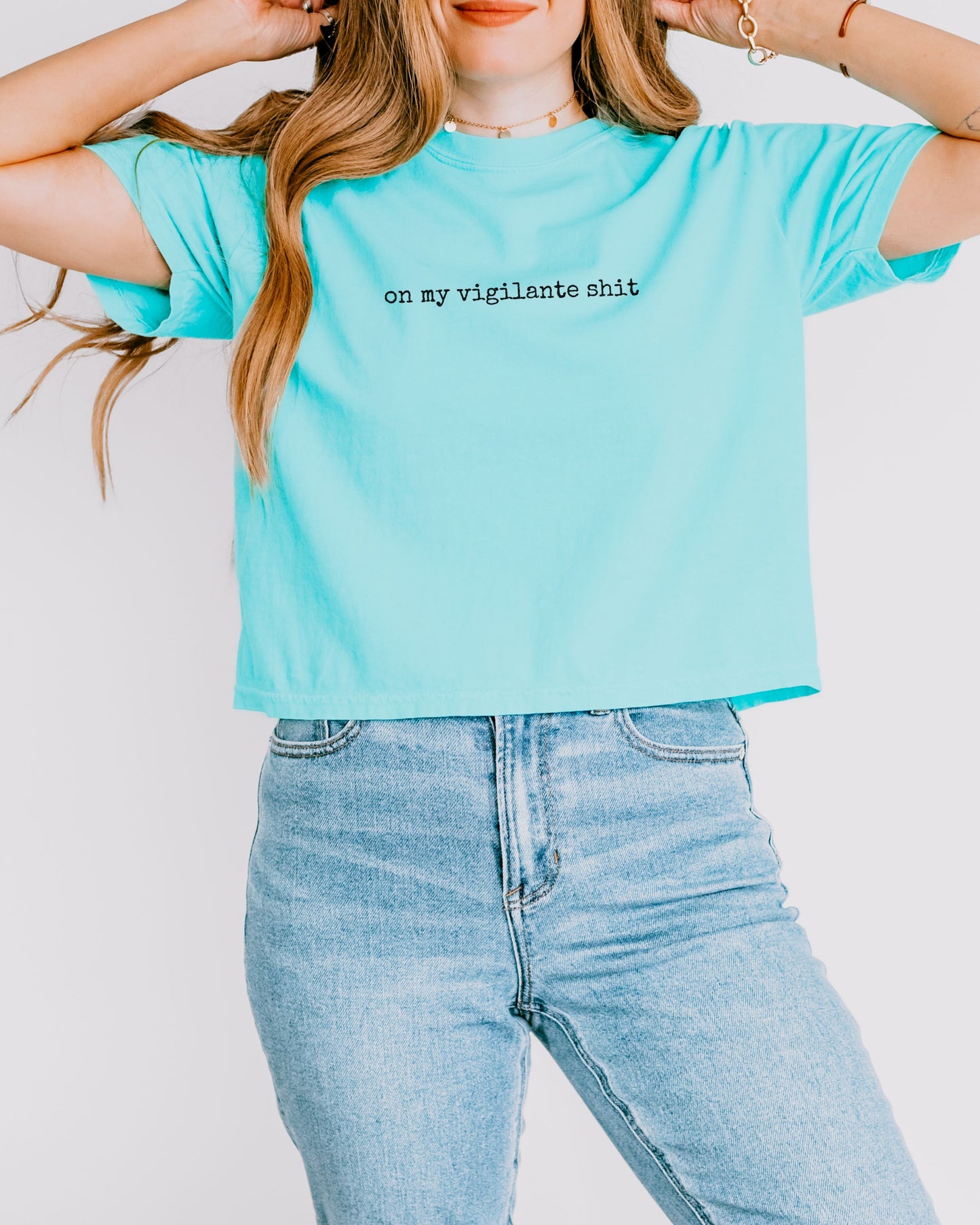 Person wearing a light blue t-shirt with on my vigilante shit text in black font and jeans on a plain background