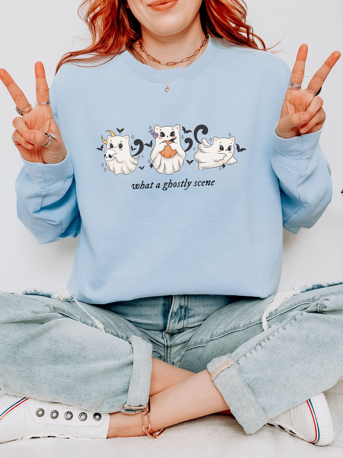 Person wearing a light blue sweatshirt with ghost illustrations and text, sitting on a white floor.