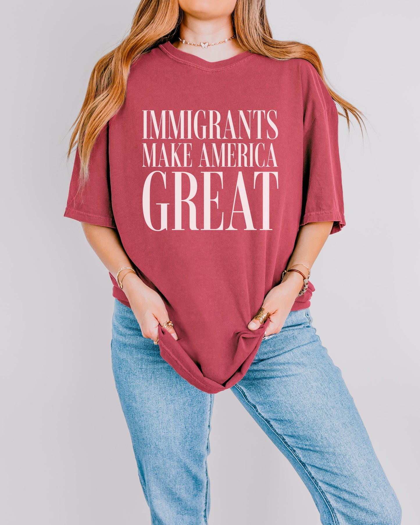 Person wearing a maroon t-shirt with 'IMMIGRANTS MAKE AMERICA GREAT' text on a plain background