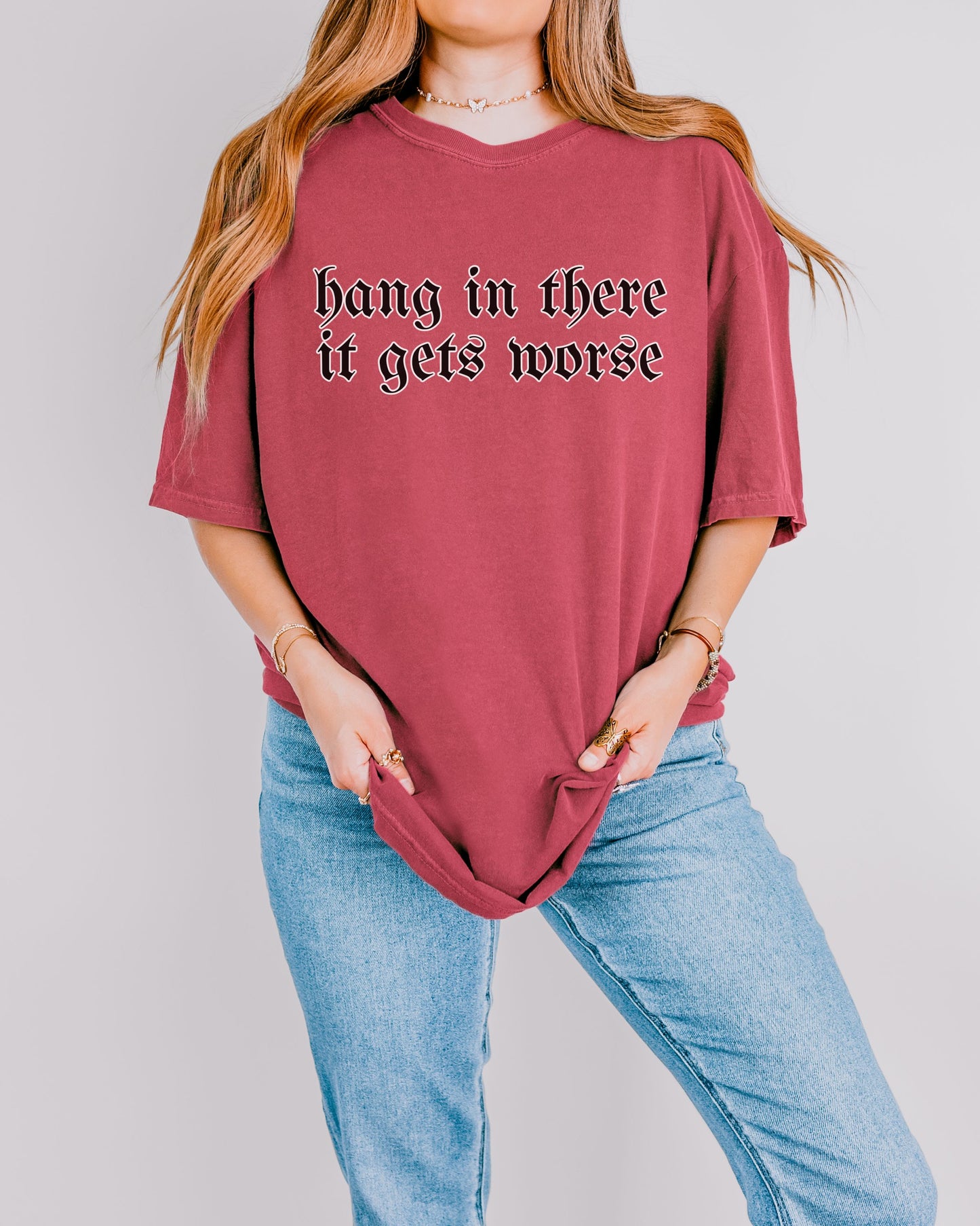 Person wearing a maroon t-shirt with text 'hang in there it gets worse' on a plain background