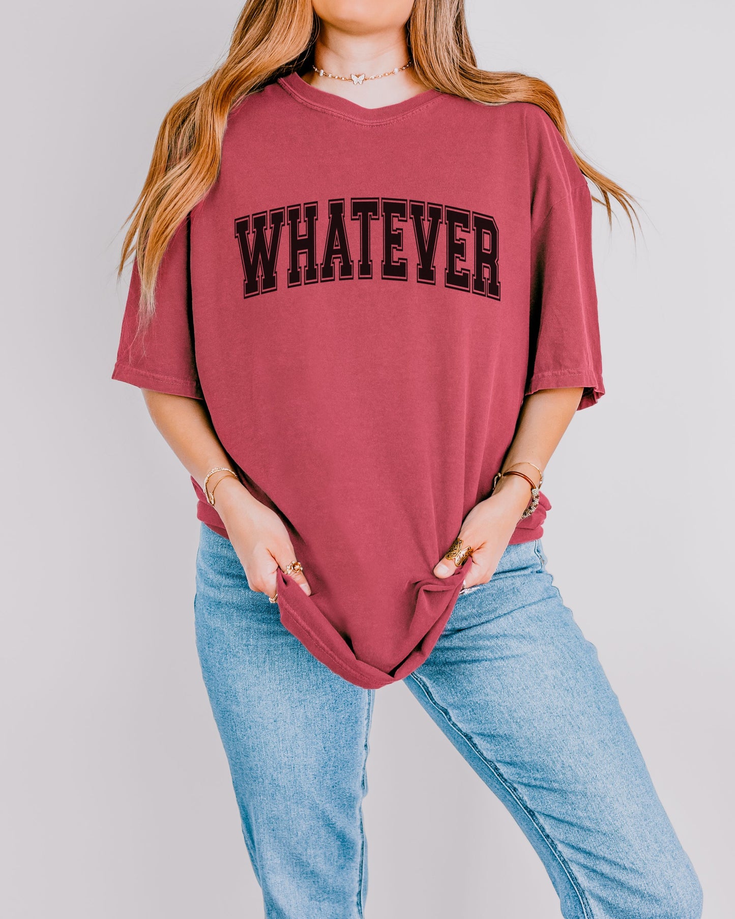 Person wearing a maroon t-shirt with 'WHATEVER' text and blue jeans on a plain background