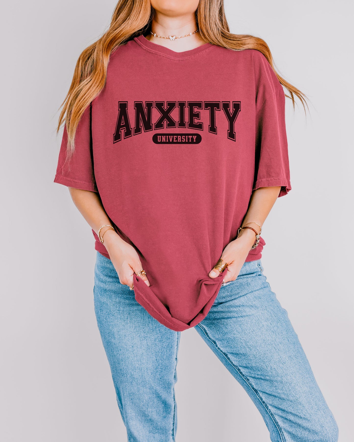 Person wearing a maroon t-shirt with 'ANXIETY UNIVERSITY' text on a plain background