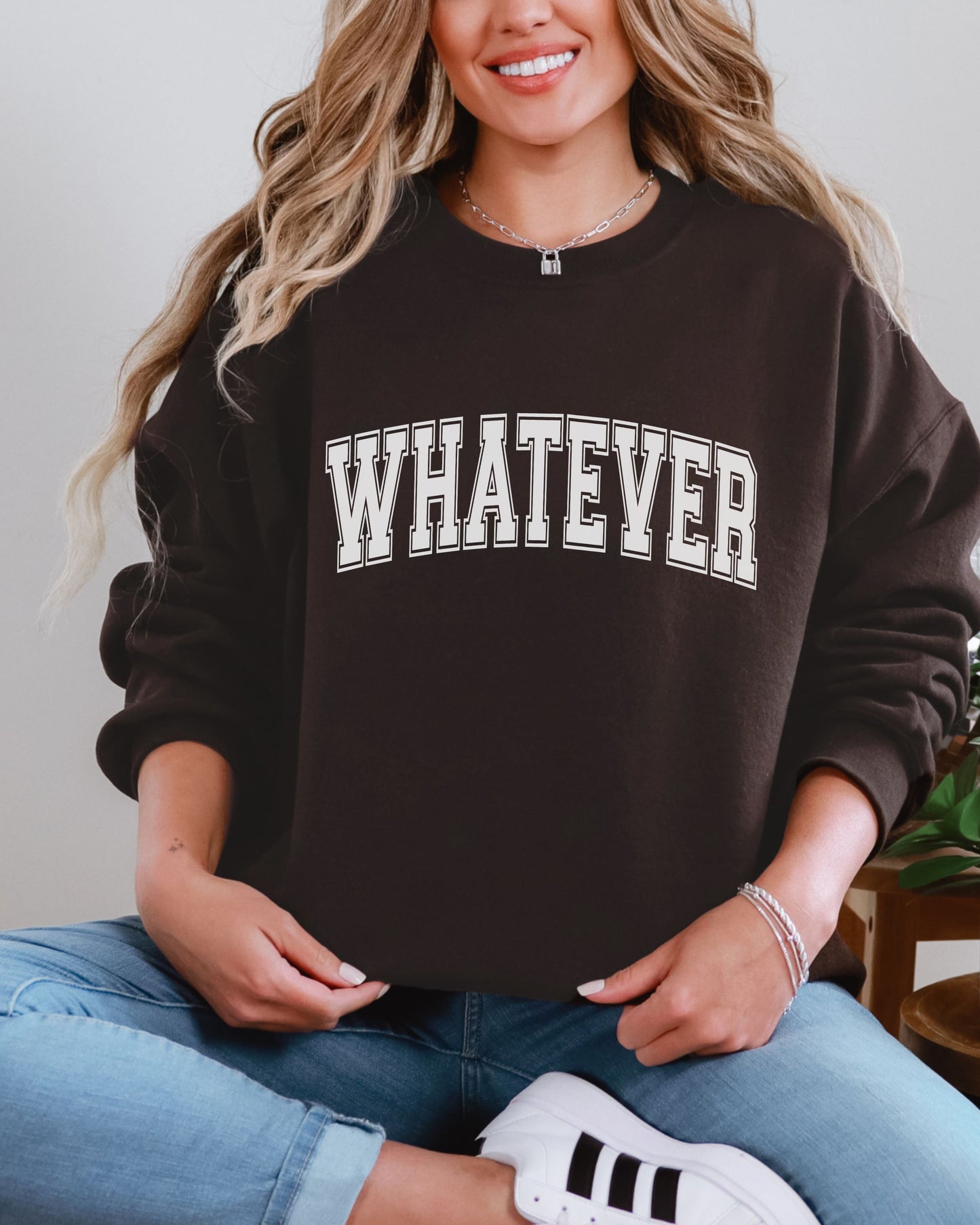 Person wearing a black sweatshirt with 'WHATEVER' text, sitting against a neutral background.