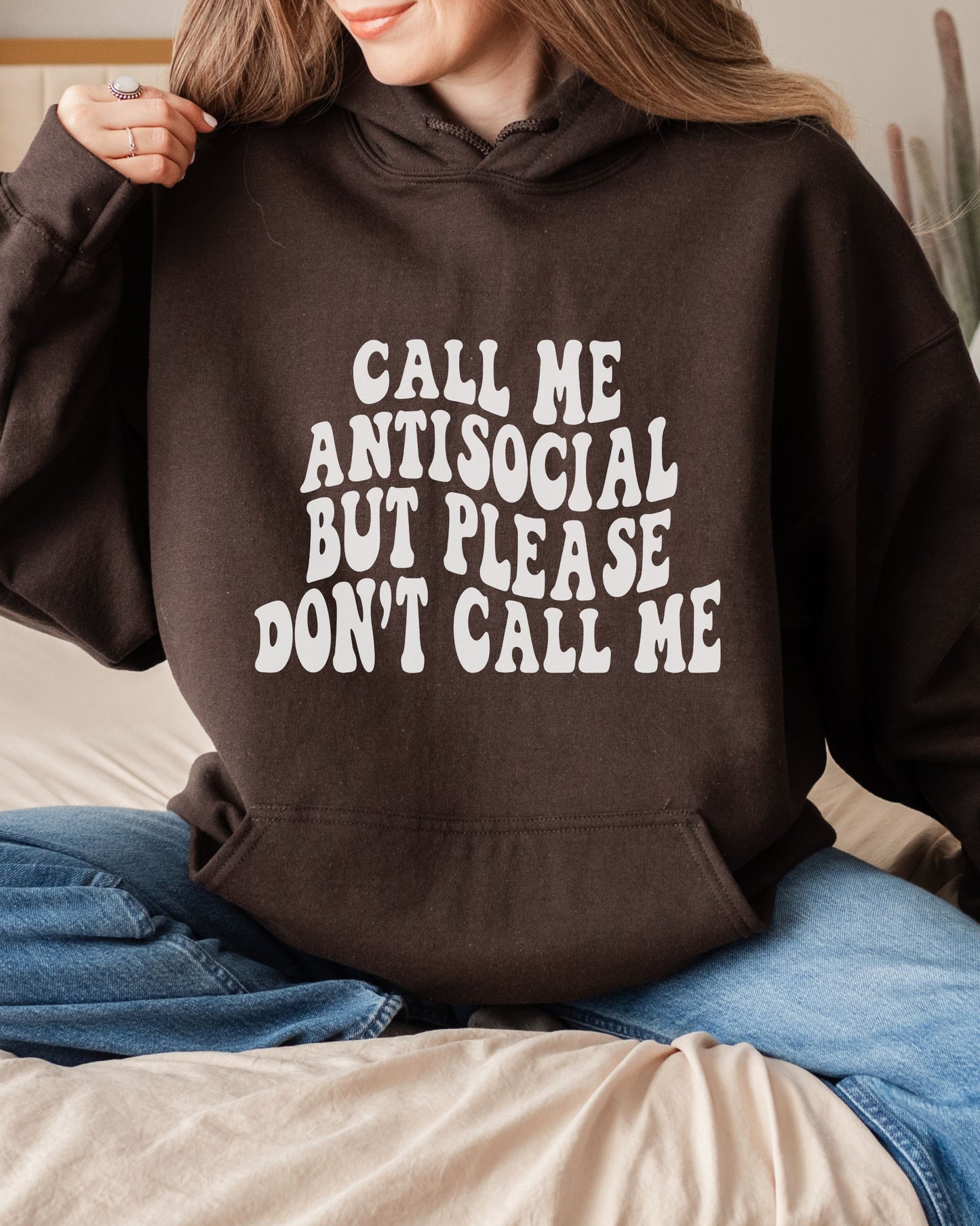 Person wearing a brown hoodie with text 'Call me antisocial but please don't call me' in a casual setting.