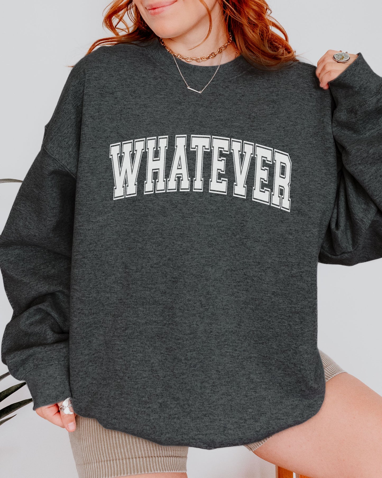 Person wearing a dark gray sweatshirt with 'WHATEVER' text on a plain background