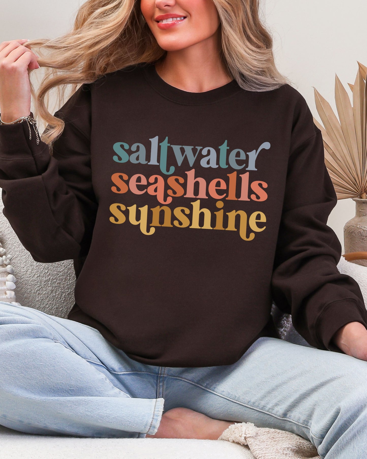 Person wearing a brown sweatshirt with 'saltwater seashells sunshine' text.