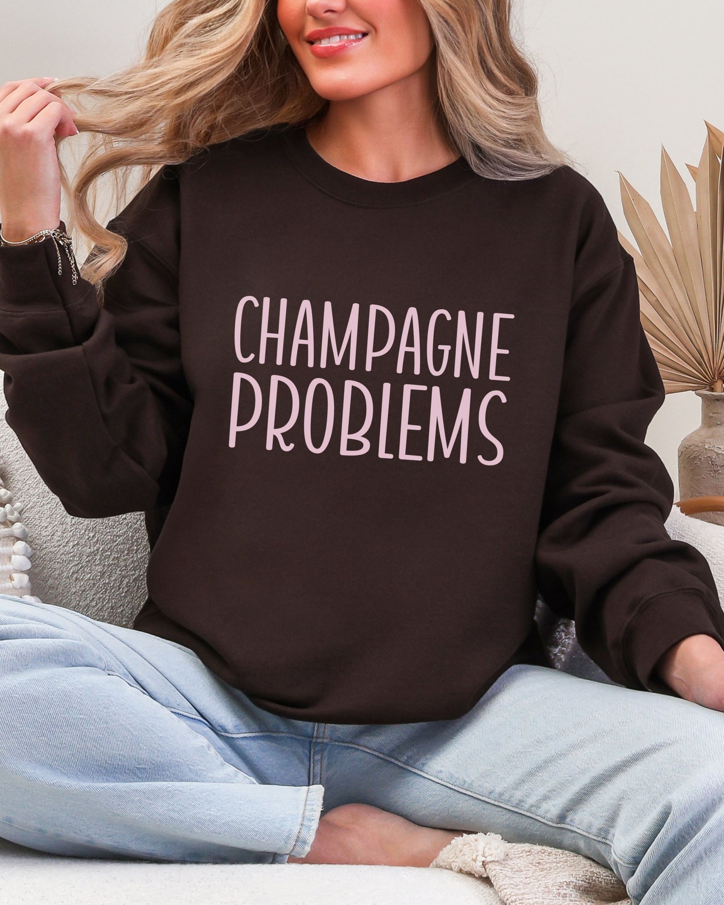 Person wearing a brown sweatshirt with 'CHAMPAGNE PROBLEMS' text, sitting on a couch.