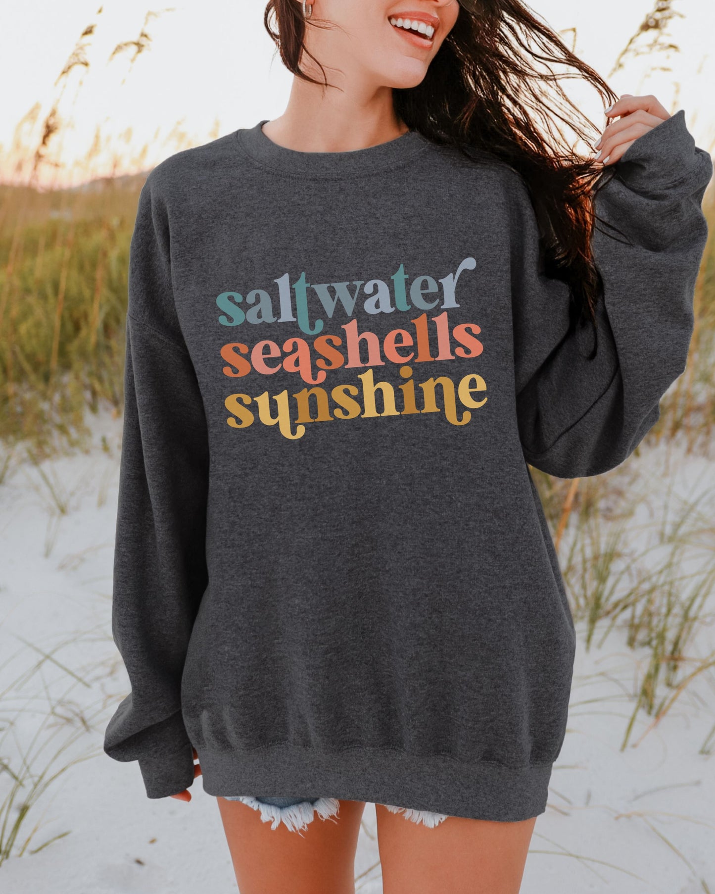 Person wearing a dark gray sweatshirt with colorful text in a beach setting