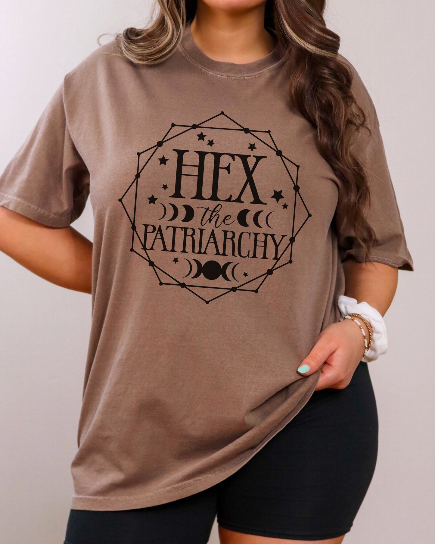 Person wearing a brown t-shirt with 'Hex the Patriarchy' text design.