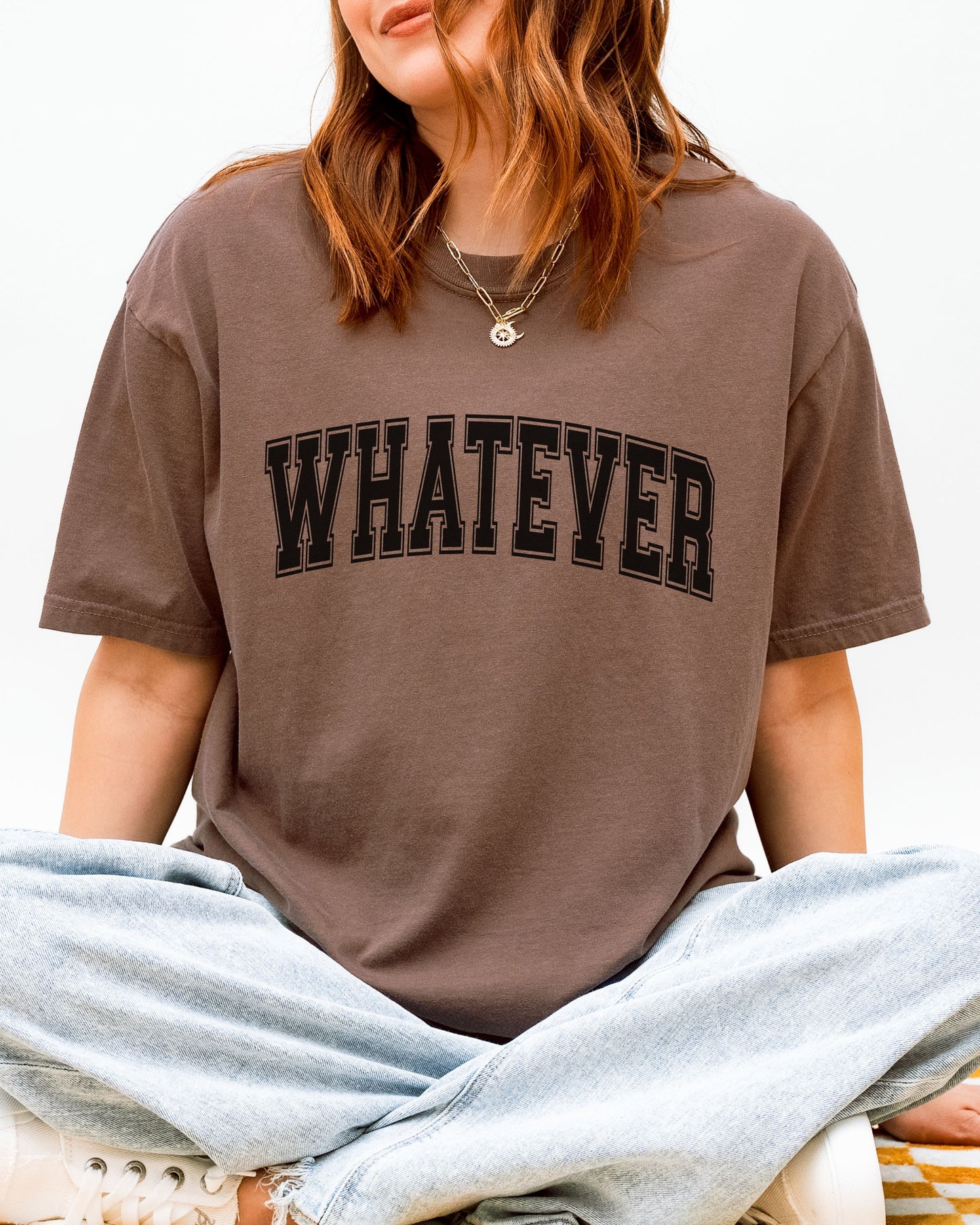 Person wearing a brown t-shirt with 'WHATEVER' text on a white background