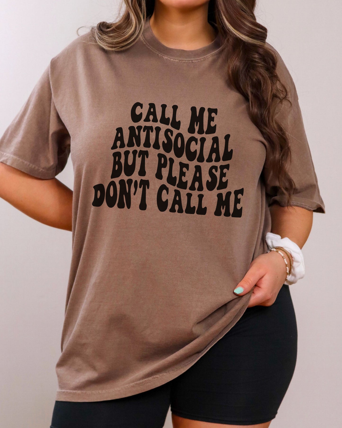 Person wearing a brown t-shirt with text 'Call me antisocial but please don't call me' on a plain background