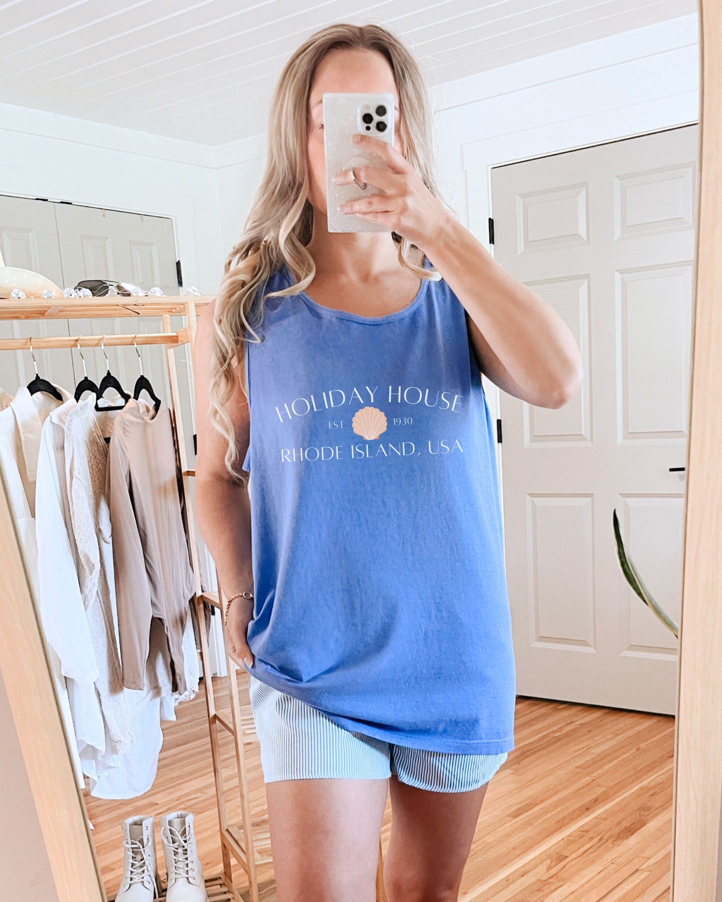 Person wearing a blue tank top with text in a room with clothes and a mirror.
