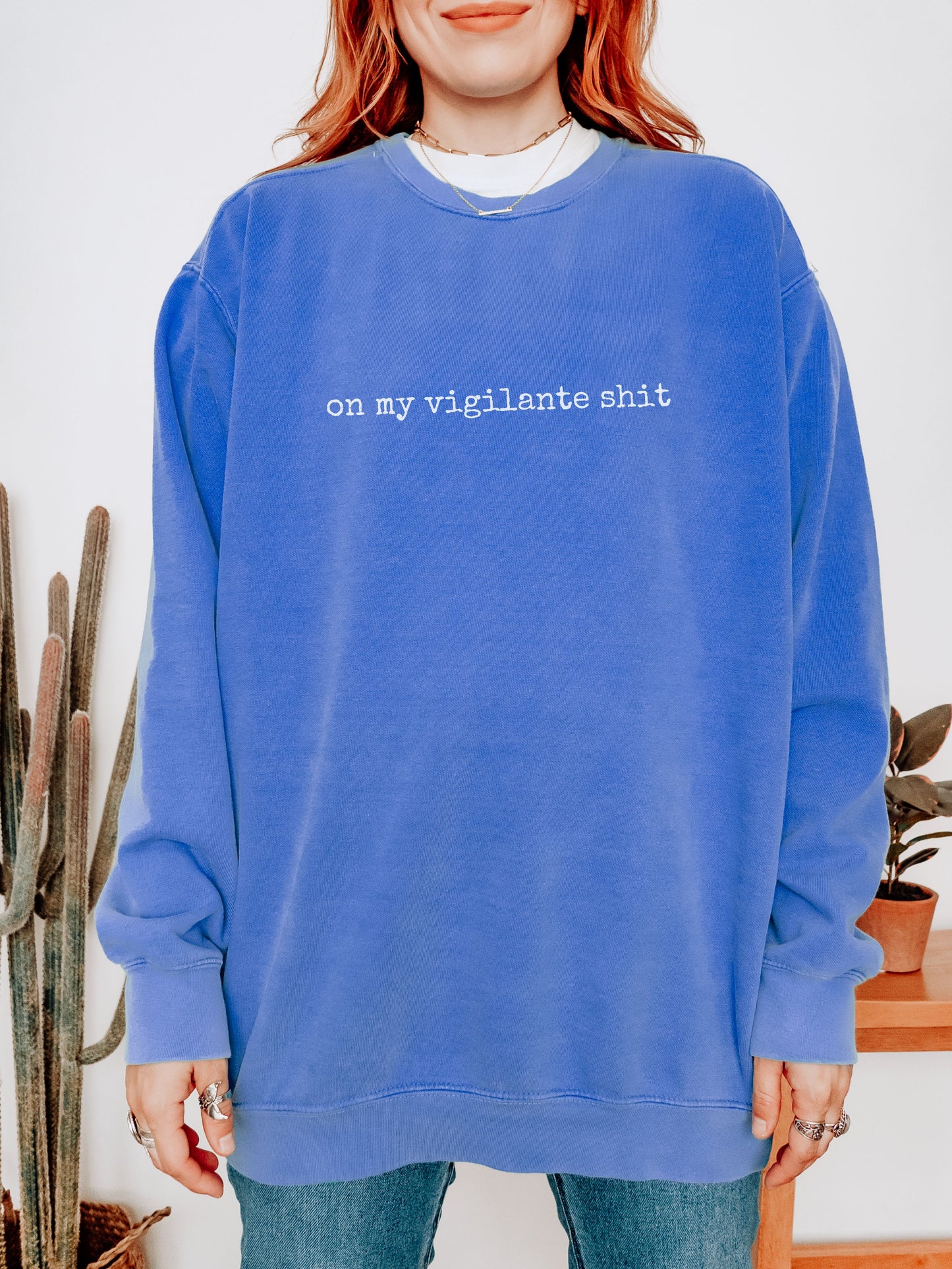 Person wearing a blue sweatshirt with text, standing indoors with plants in the background