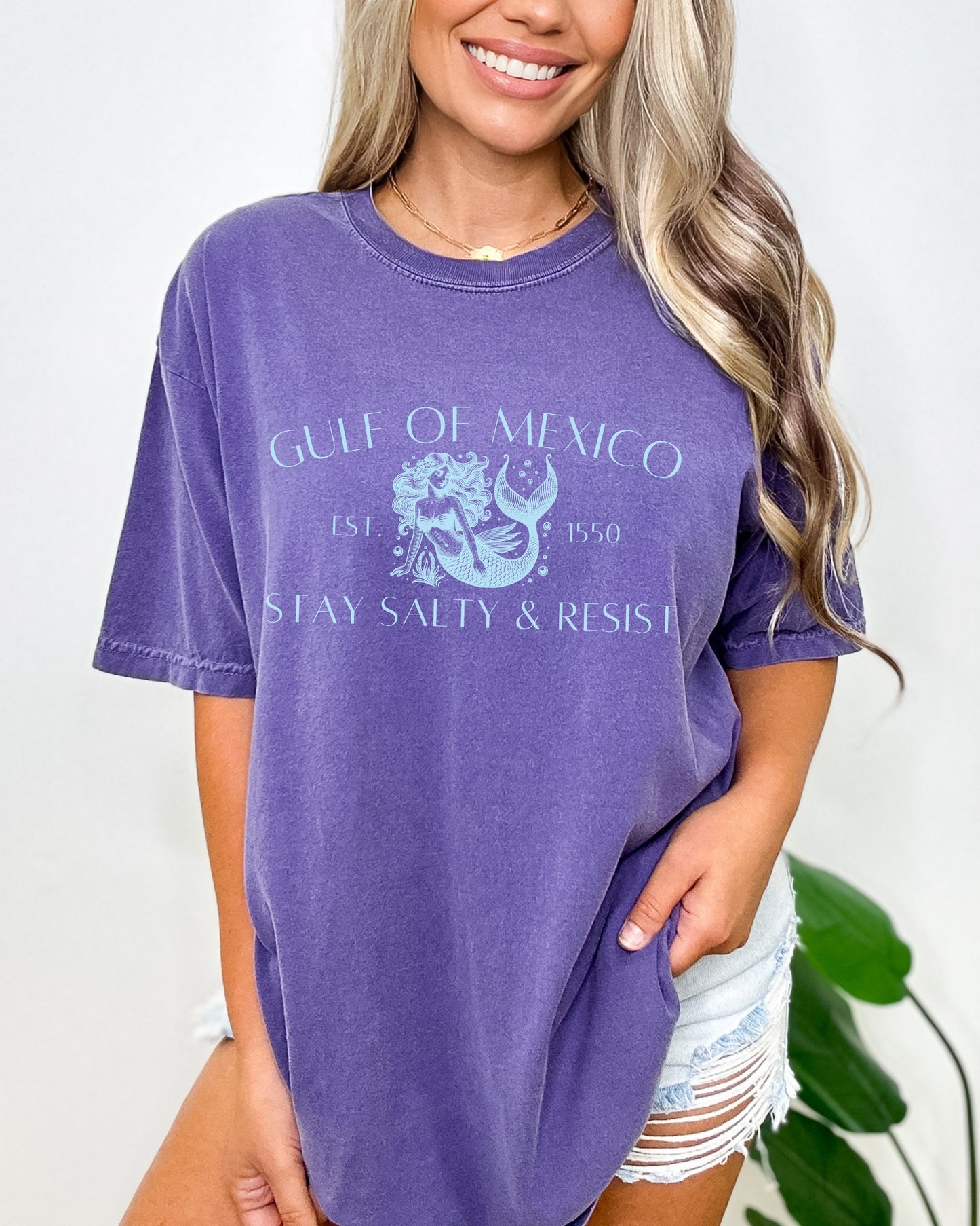 Woman wearing a purple t-shirt with 'Gulf of Mexico' design, standing against a white background.