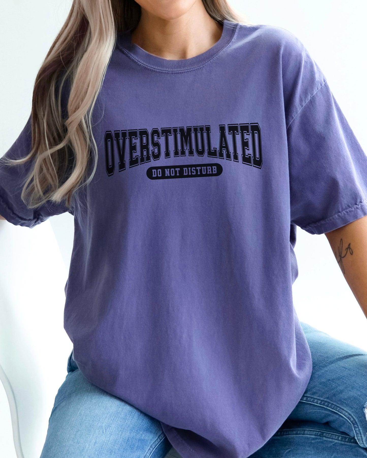 Person wearing a purple t-shirt with 'OVERSTIMULATED DO NOT DISTURB' text.