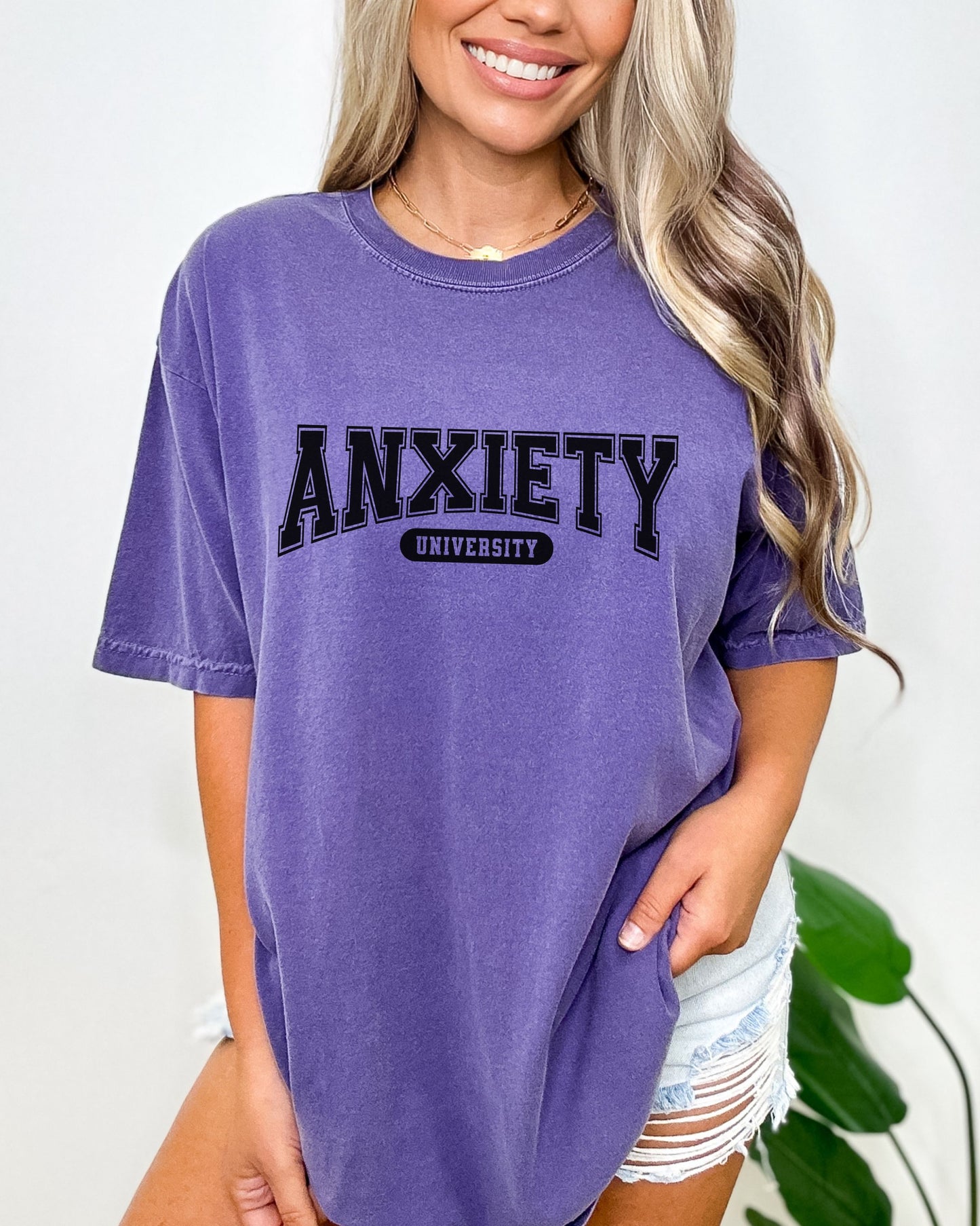 Person wearing a purple t-shirt with 'ANXIETY UNIVERSITY' text on a plain background