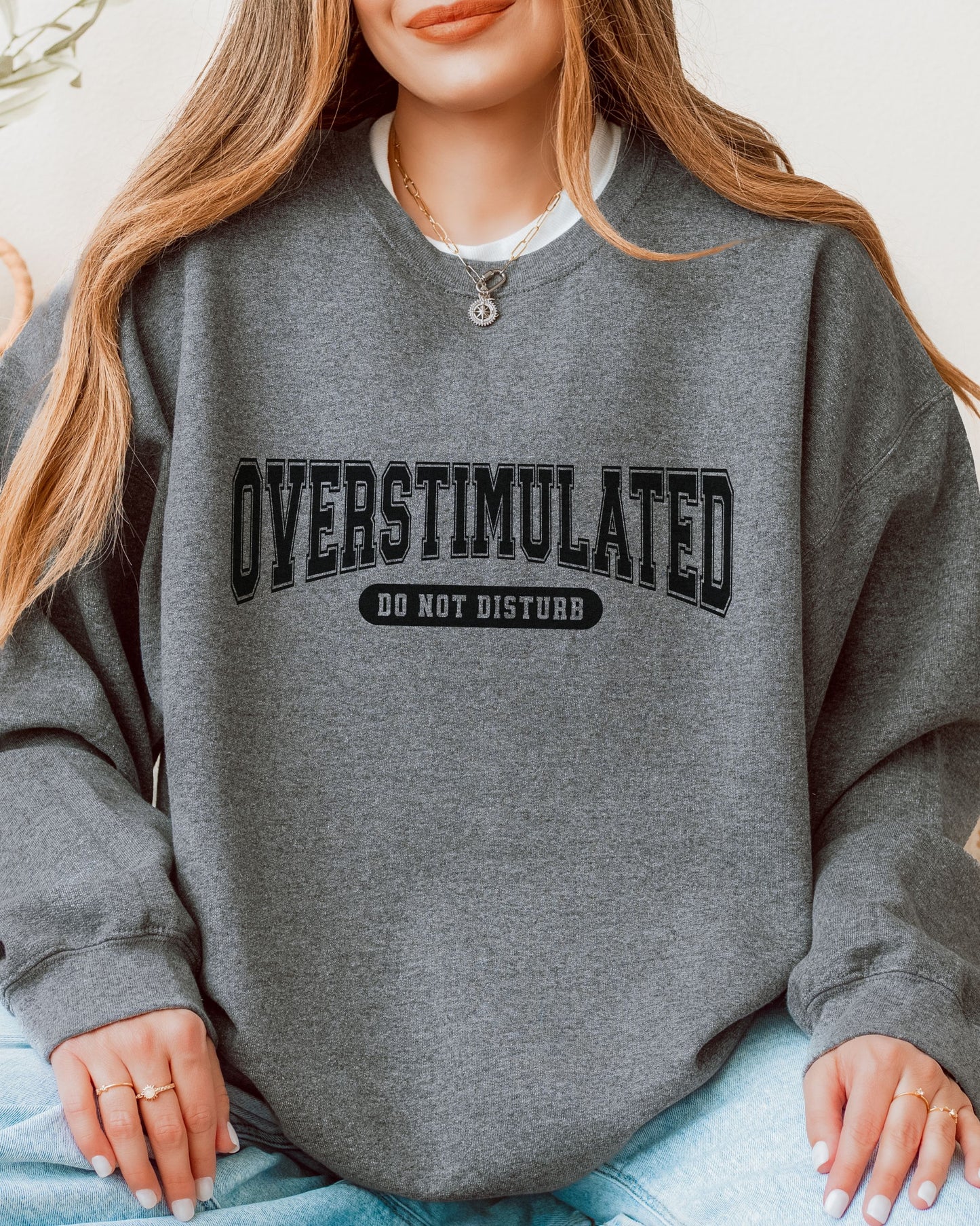 Person wearing a gray sweatshirt with 'OVERSTIMULATED DO NOT DISTURB' text.