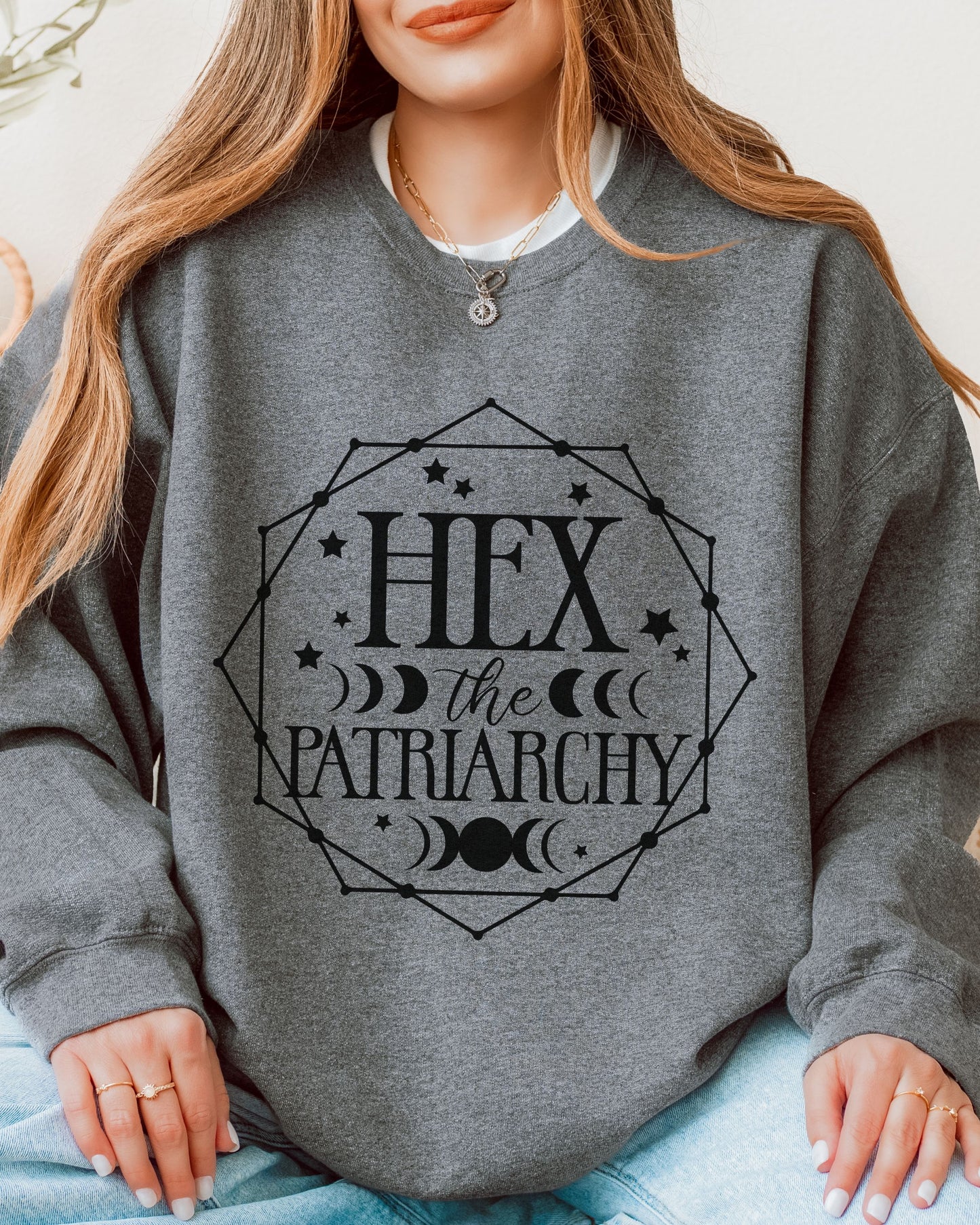Person wearing a gray sweatshirt with 'Hex the Patriarchy' text design.