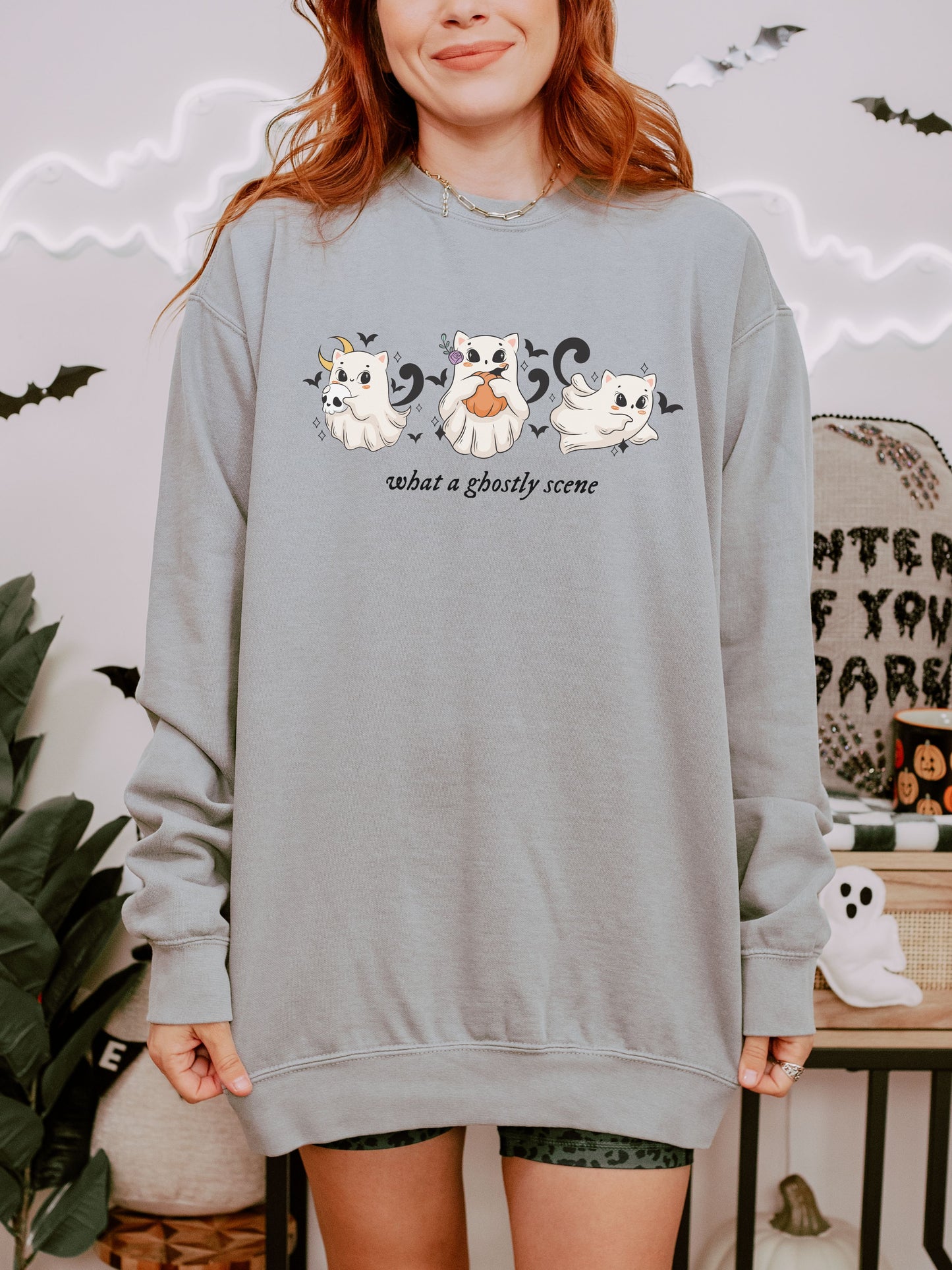 Person wearing a gray sweatshirt with ghost designs and text in a Halloween-themed setting.