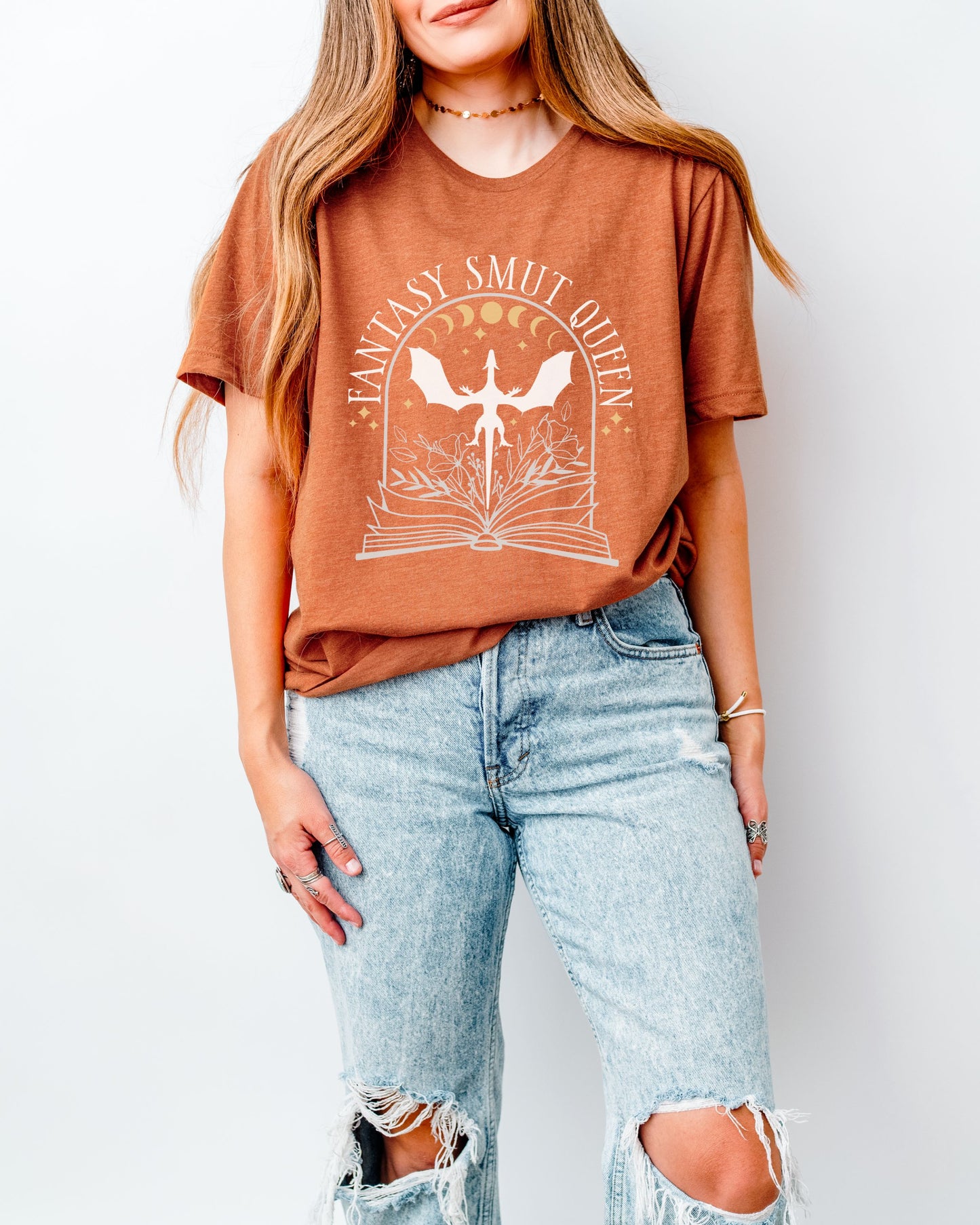 Person wearing an orange t-shirt with a graphic design and ripped jeans on a white background