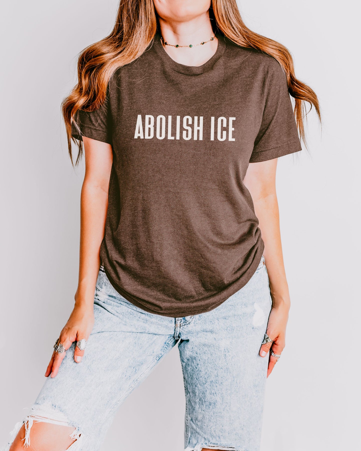 Person wearing a brown t-shirt with 'ABOLISH ICE' text against a plain background