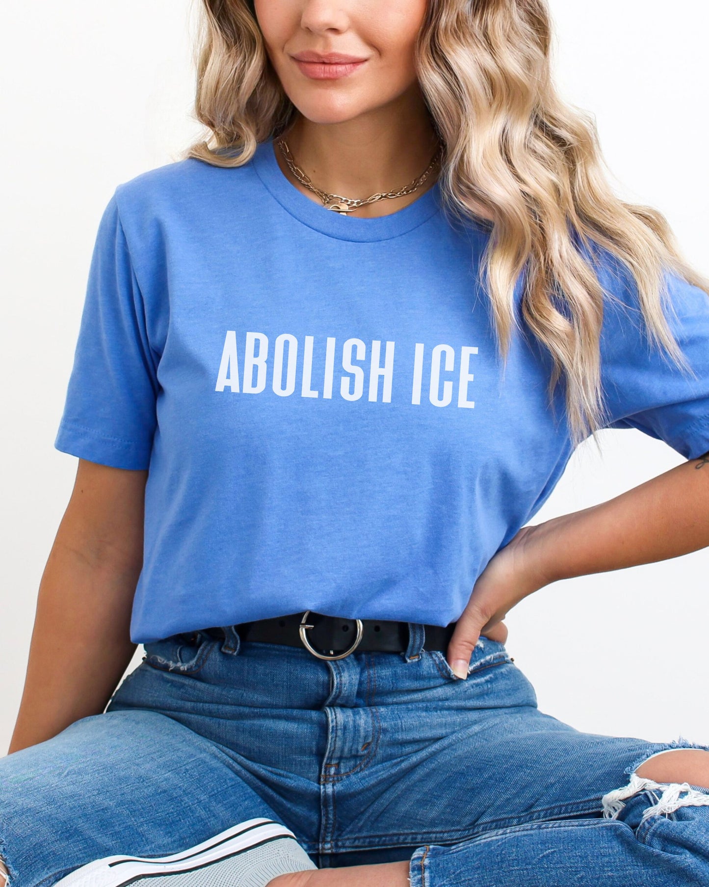 Person wearing a blue t-shirt with 'ABOLISH ICE' text on a plain background