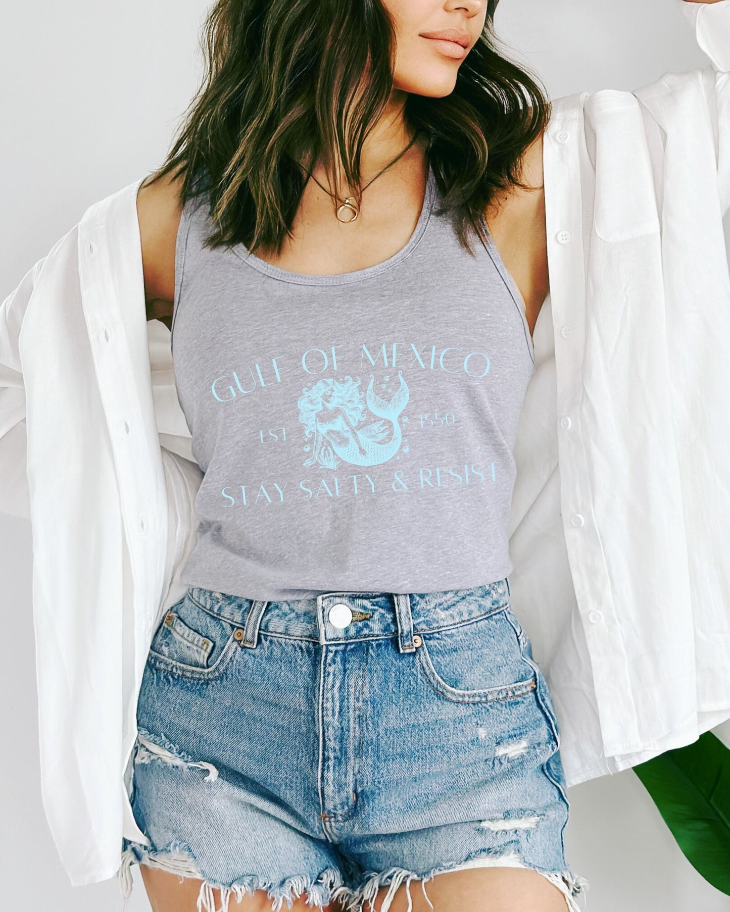 Person wearing a gray tank top with graphic design and denim shorts on a plain background