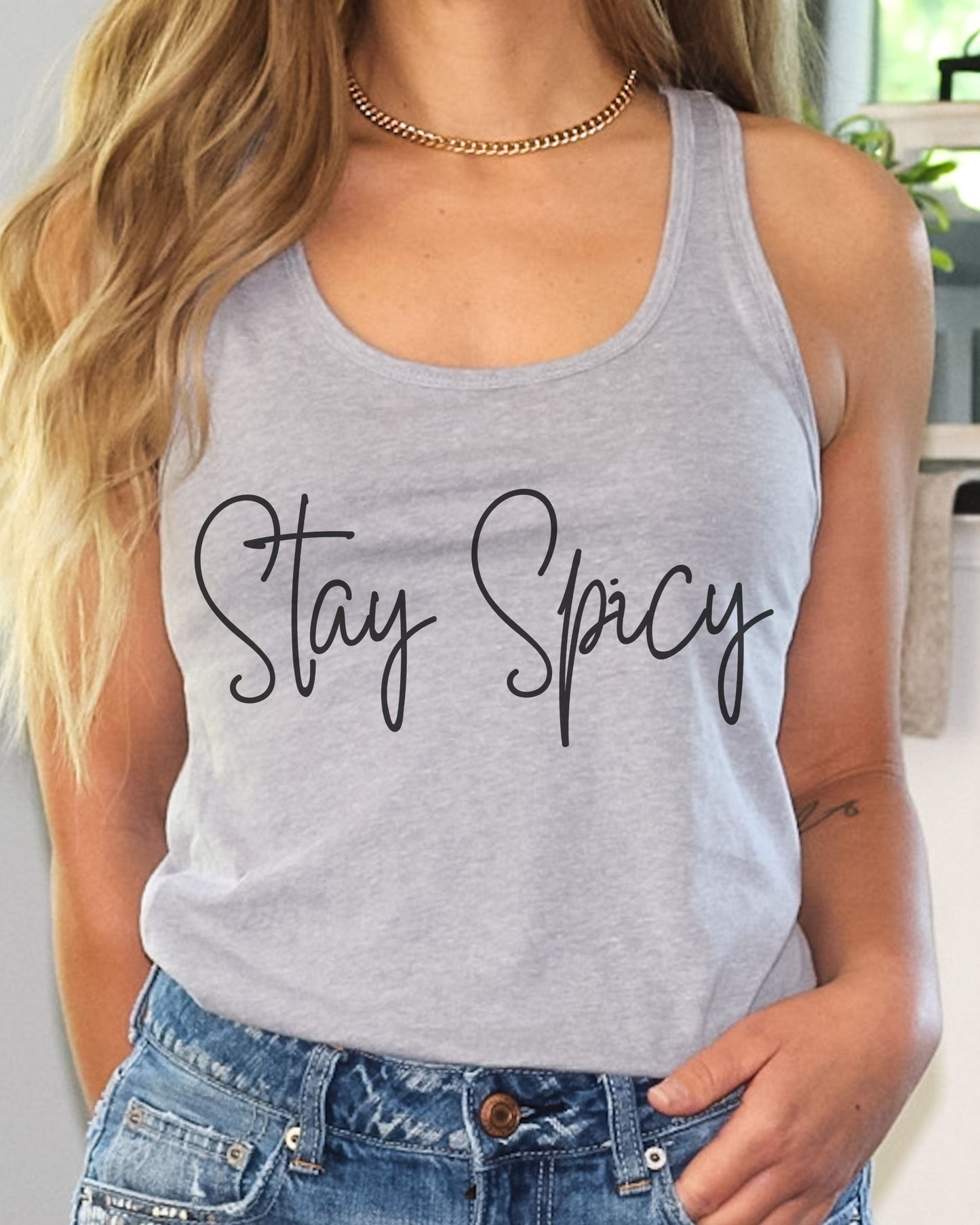 Person wearing a gray tank top with 'Stay Spicy' text, paired with blue jeans.