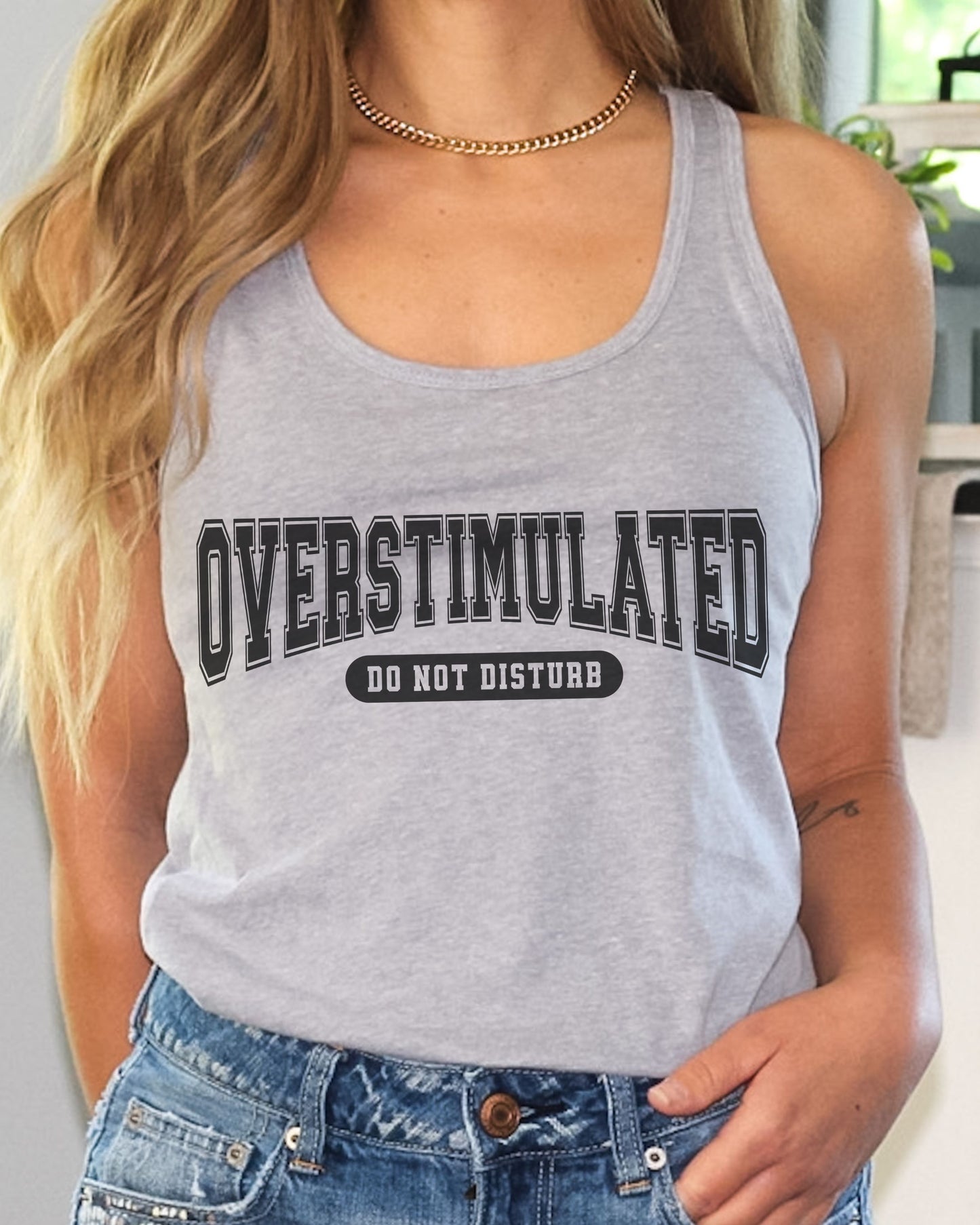 Person wearing a gray tank top with 'OVERSTIMULATED DO NOT DISTURB' text.